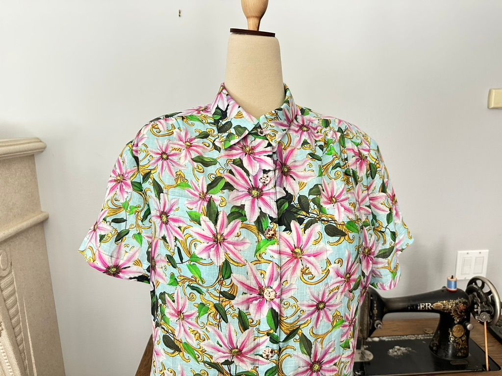 Floral shirt on a mannequin in front of a sewing machine. The shirt is light blue with pink flowers.