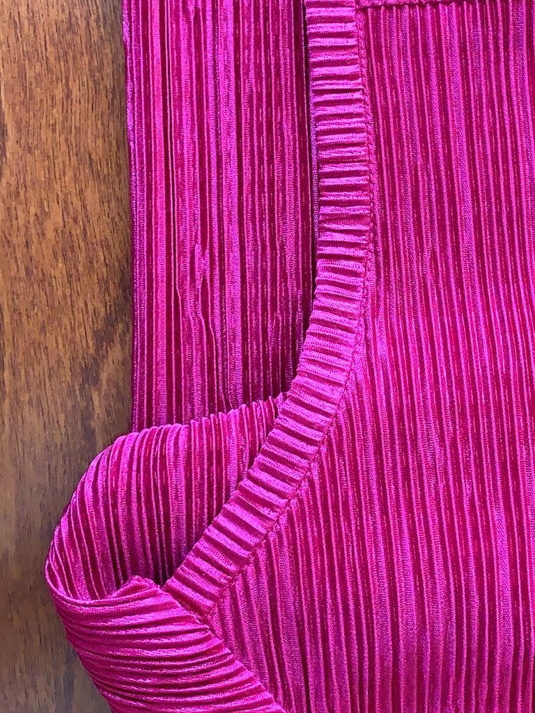 Close-up of a vibrant pink pleated fabric, showing the texture of the material, likely part of a garment.