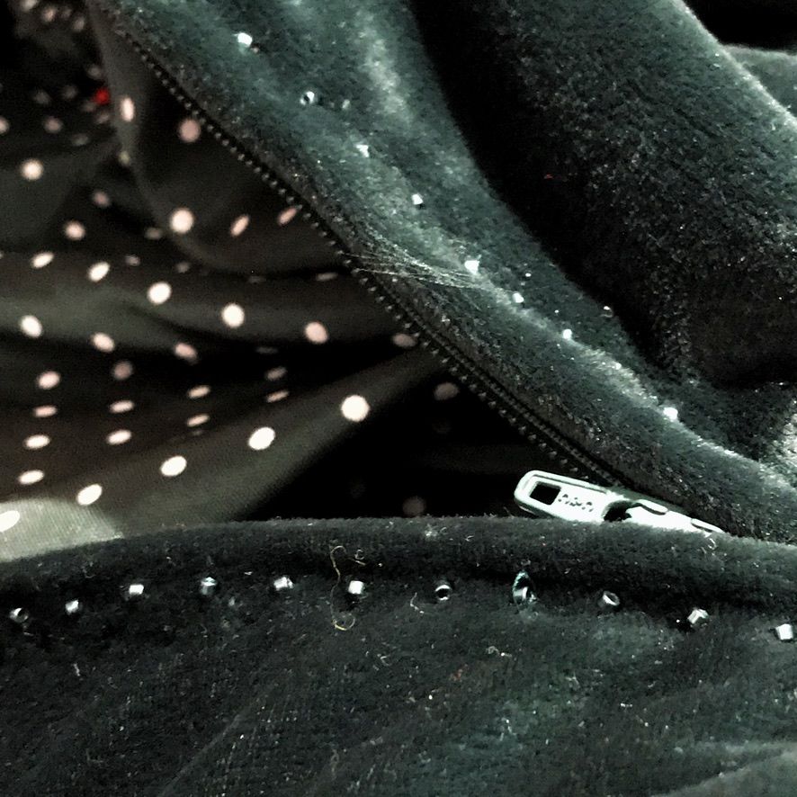 Black velvet fabric with a zipper and small embellishments, polka dot lining visible.