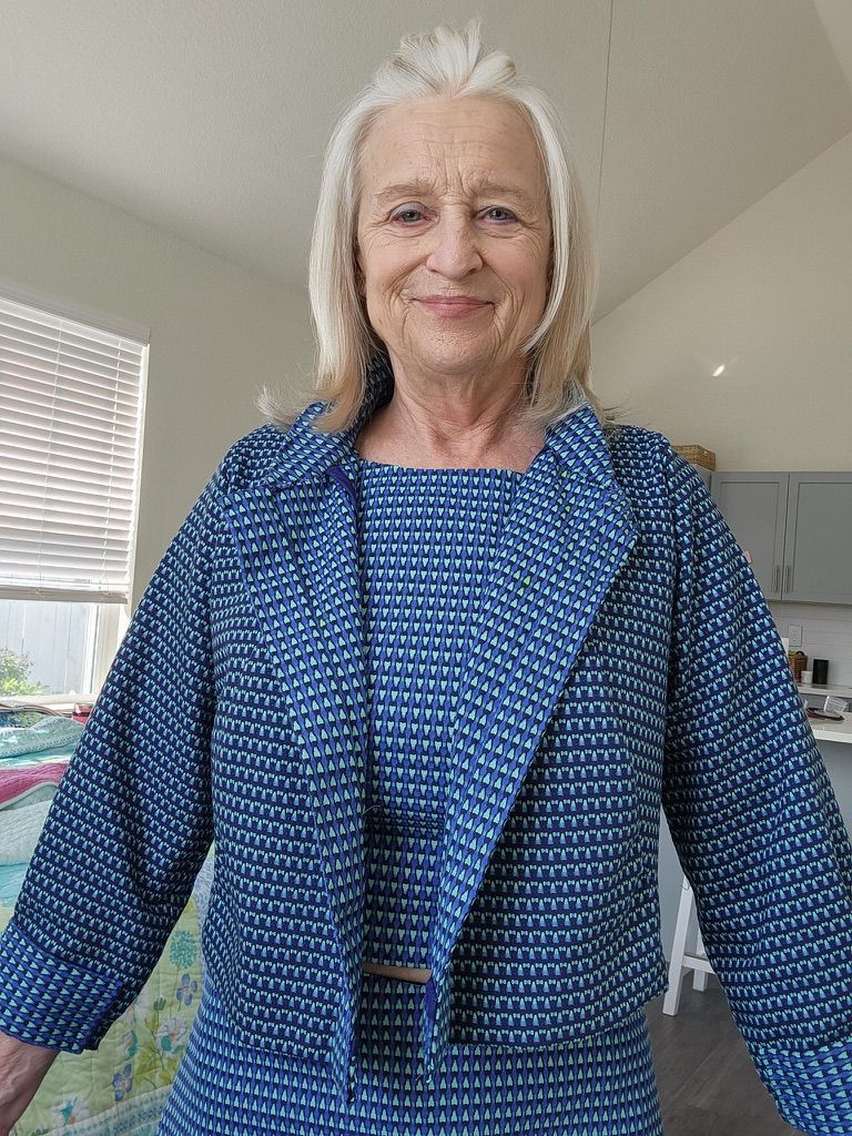 Woman wearing a matching blue jacket and dress, smiling in a bright room.