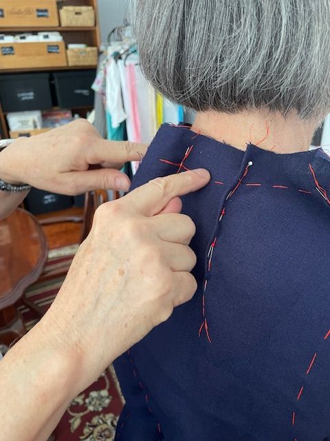 Hands pointing to the shoulder seam of a dark blue garment on a person.