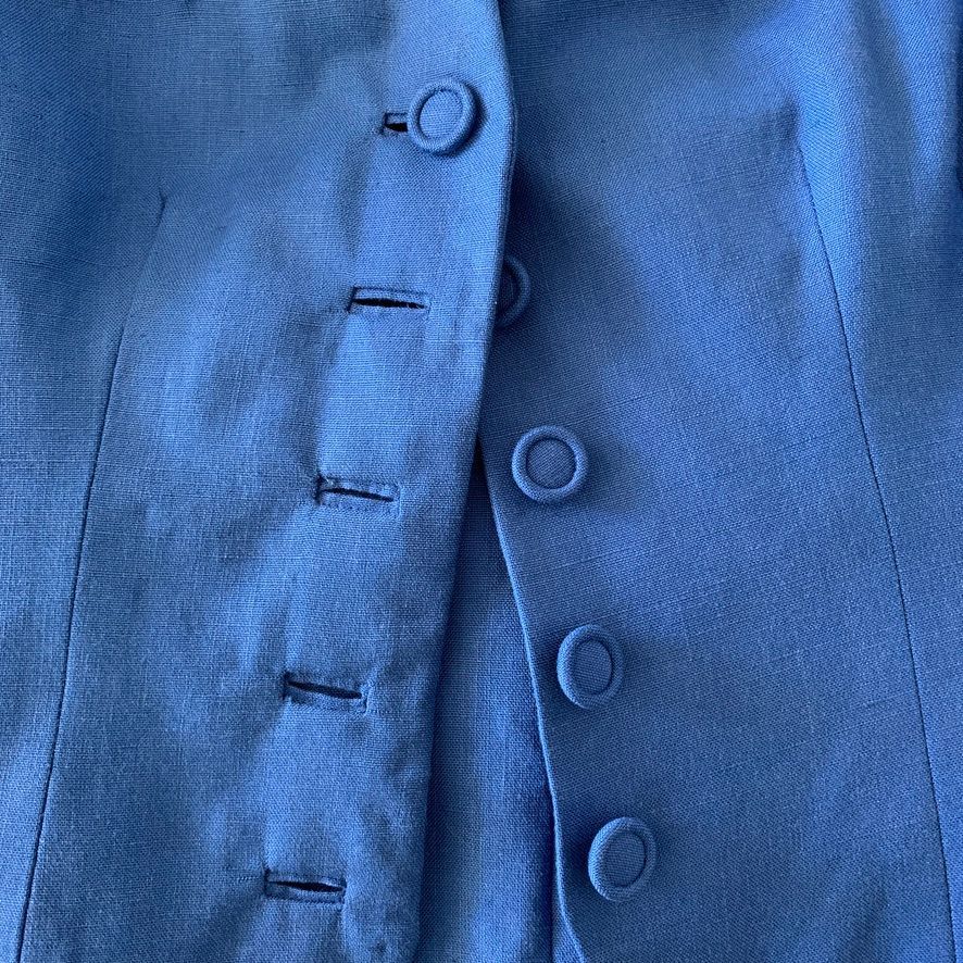 Close-up of a blue fabric garment with a button closure and four visible buttons.