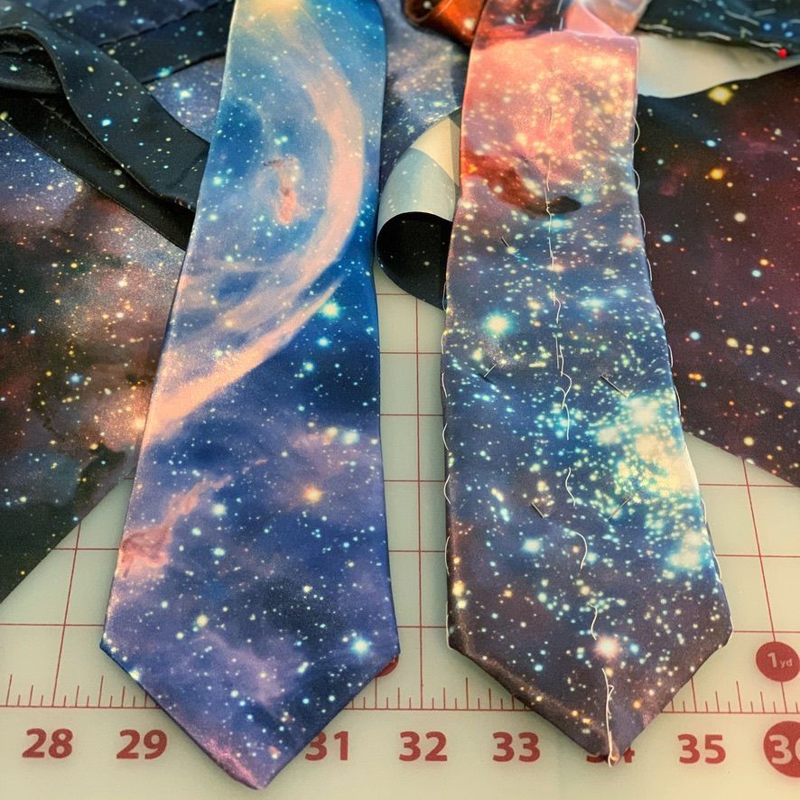 Two neckties with a galaxy print are laid out on a cutting mat.
