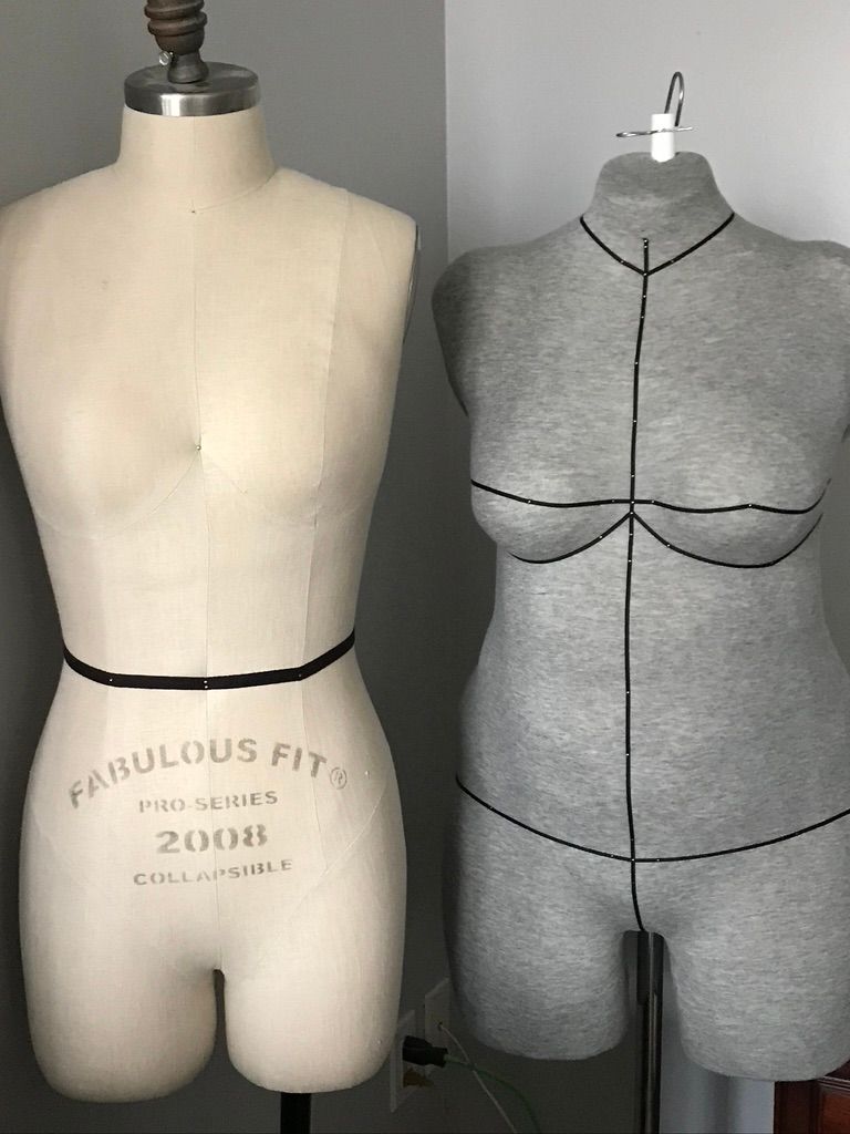 Two dressmaker's forms: one beige, one gray, marked with black lines and waist tape.
