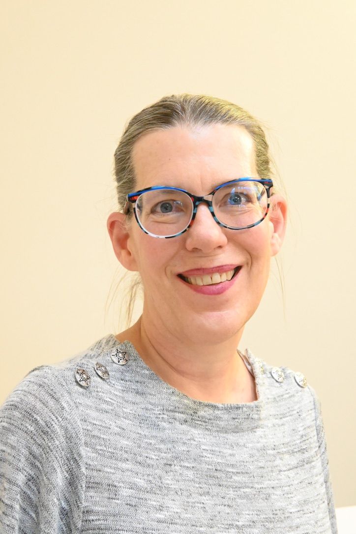 Woman wearing glasses smiles at the camera, wearing a gray sweater.