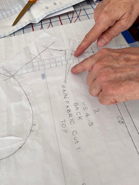 Hands pointing at a sewing pattern with lines and text, possibly guiding cutting.