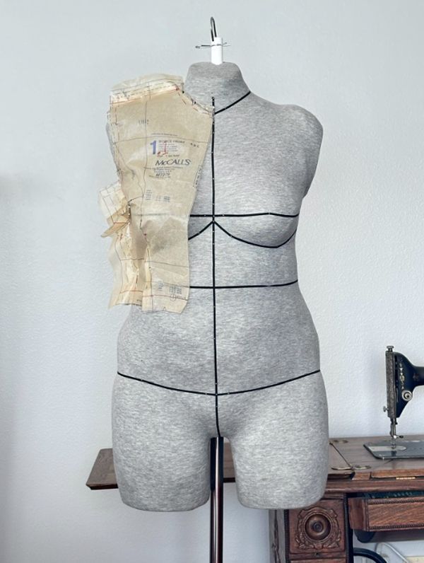 Sewing dress form with pinned beige pattern pieces in a workshop
