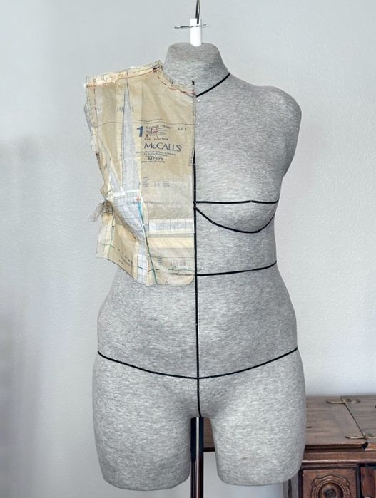 Dress form mannequin with pinned beige pattern pieces draped over one shoulder