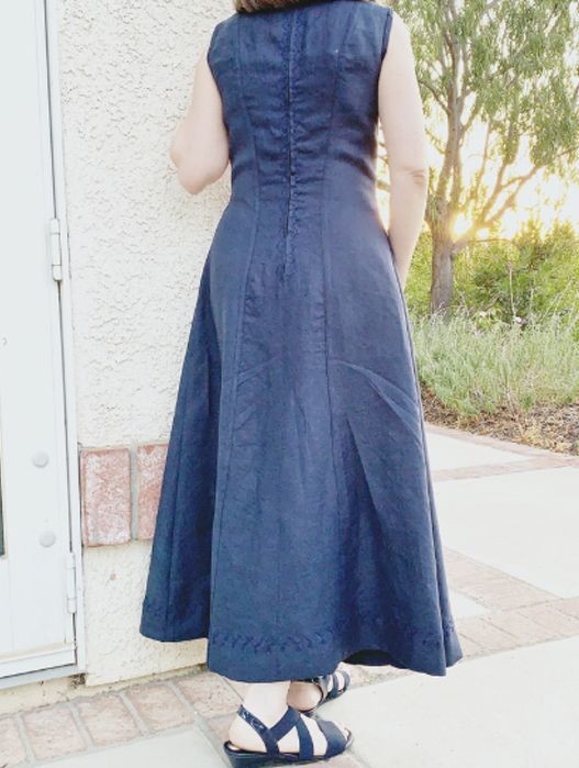 Person in a navy sleeveless dress standing outdoors beside a white wall and greenery.