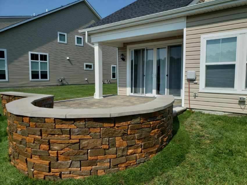 A house with a stone wall and a patio in front of it.