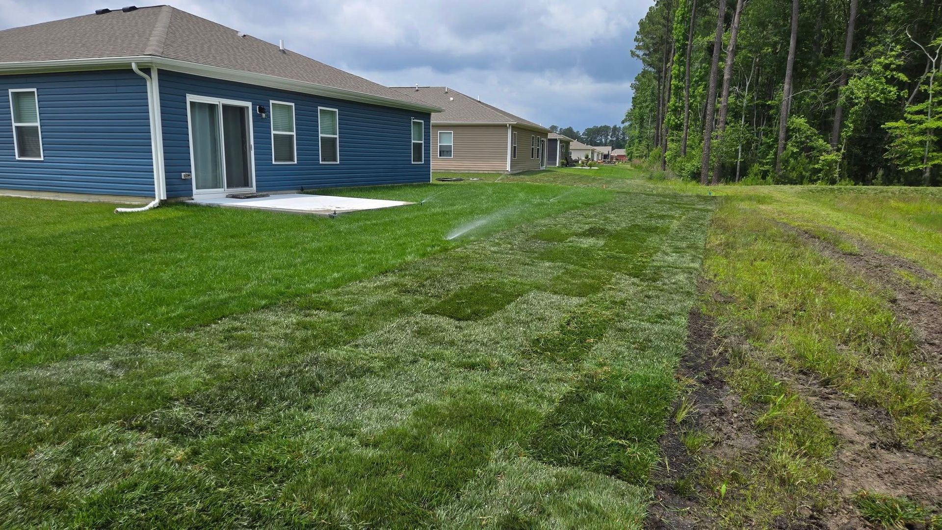 A blue house is sitting on top of a lush green lawn next to a dirt road.