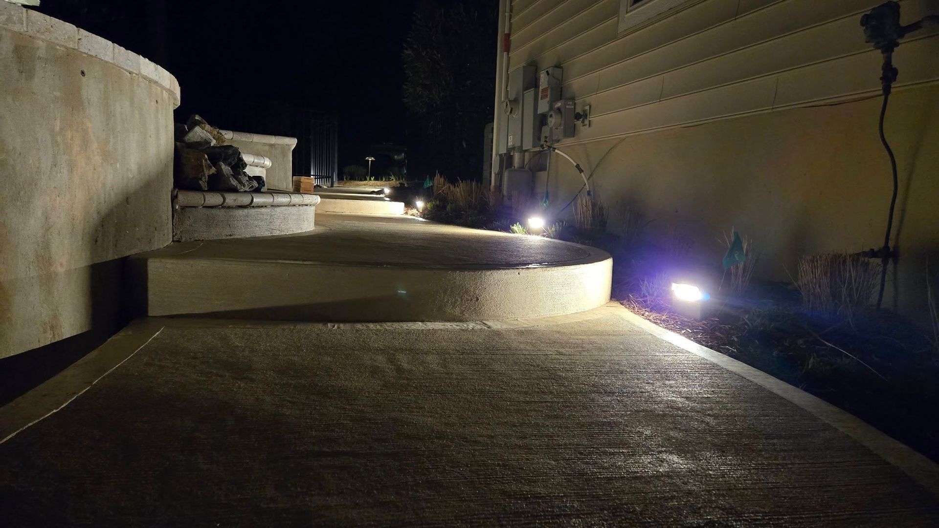 A concrete walkway with lights on the side of it at night.