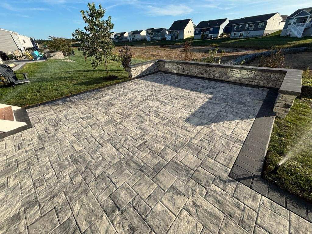 Stone patio with retaining wall, grass, and houses in the background.
