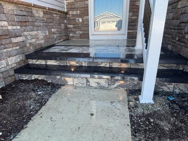 Stone steps leading to a front door with a reflecting glass window. White support post and brick veneer.