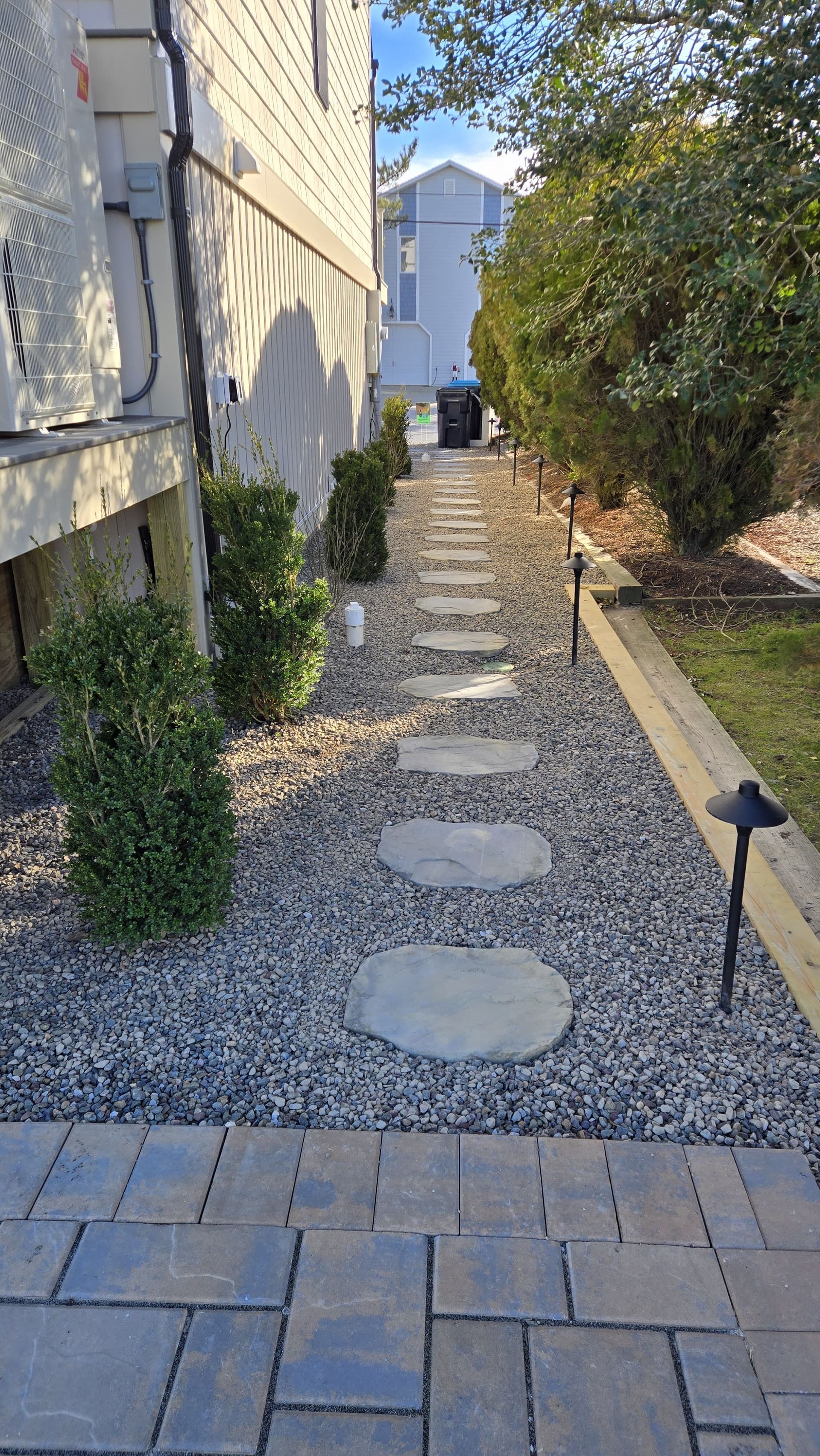 Stone path with stepping stones, flanked by bushes and gravel, beside a building.