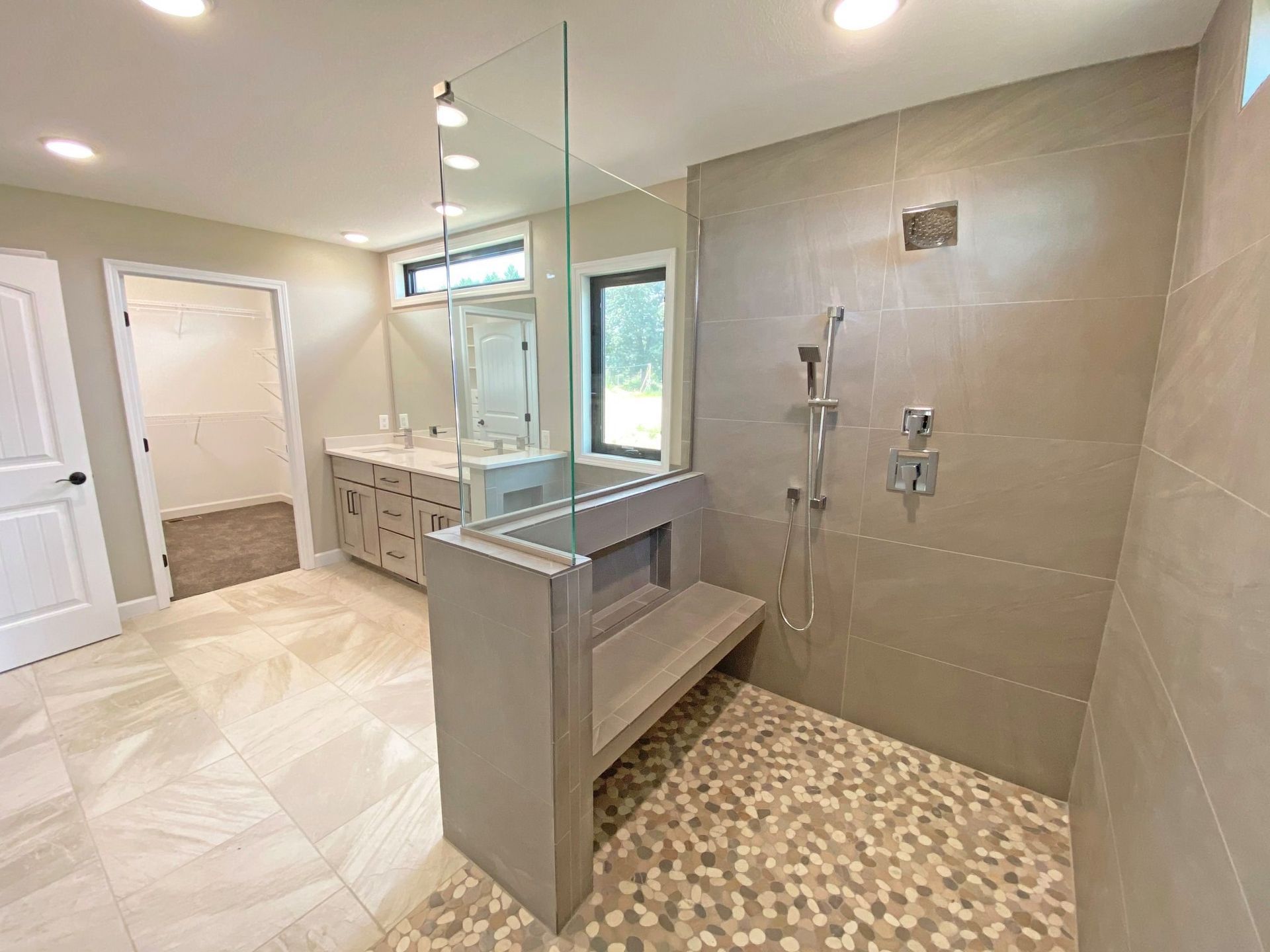 Modern bathroom with walk-in shower, glass partition, double vanity, and beige tile flooring