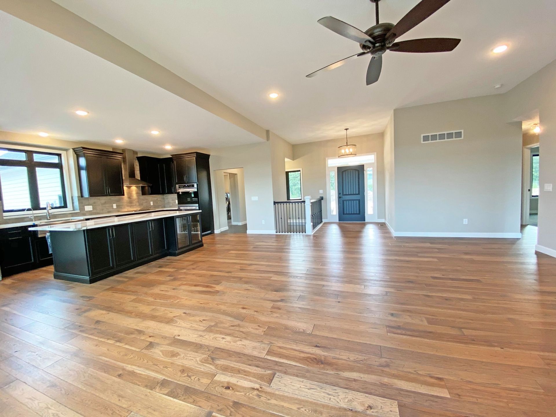 Spacious open-plan living room with hardwood floors, ceiling fan, and a kitchen with dark cabinets.