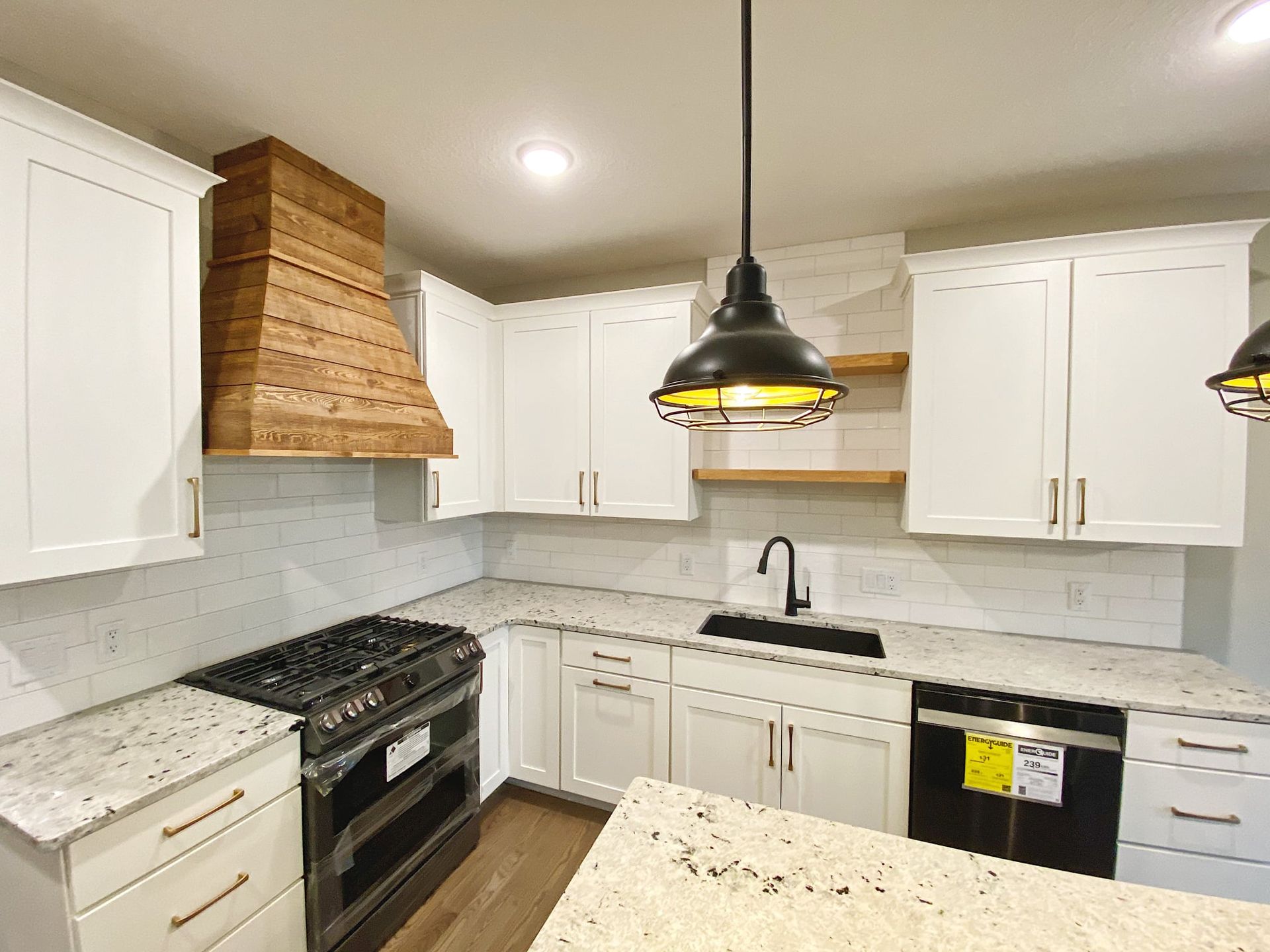 Bright modern kitchen with white cabinets, marble countertops, black stove, and wood range hood