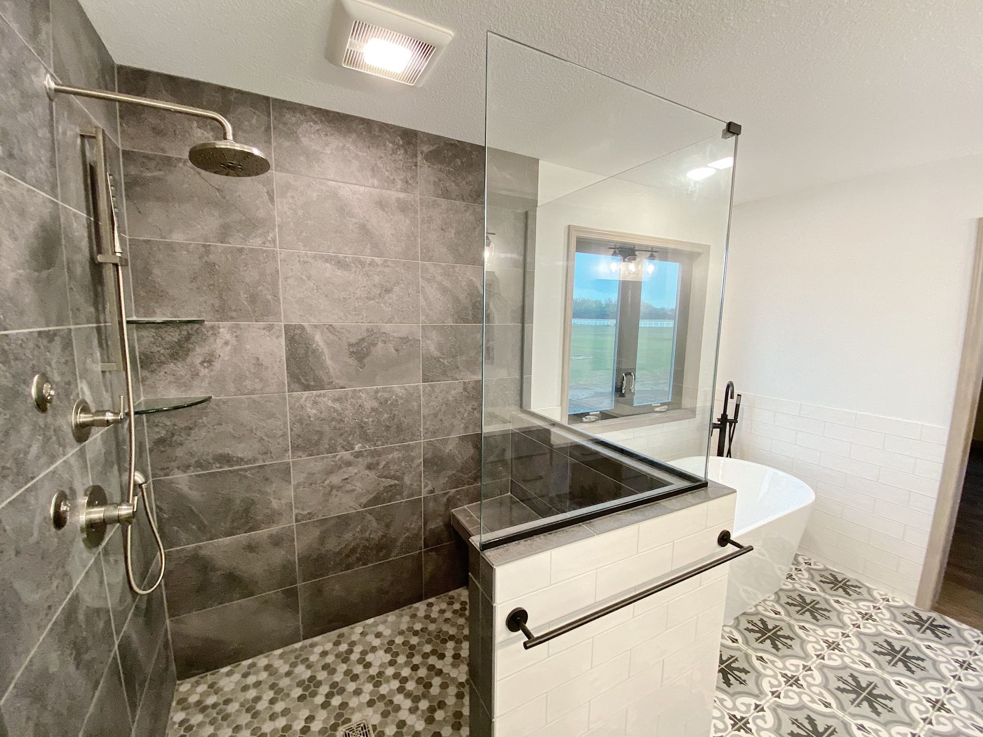 Modern bathroom with walk-in shower, glass partition, white tub, and gray tile accents