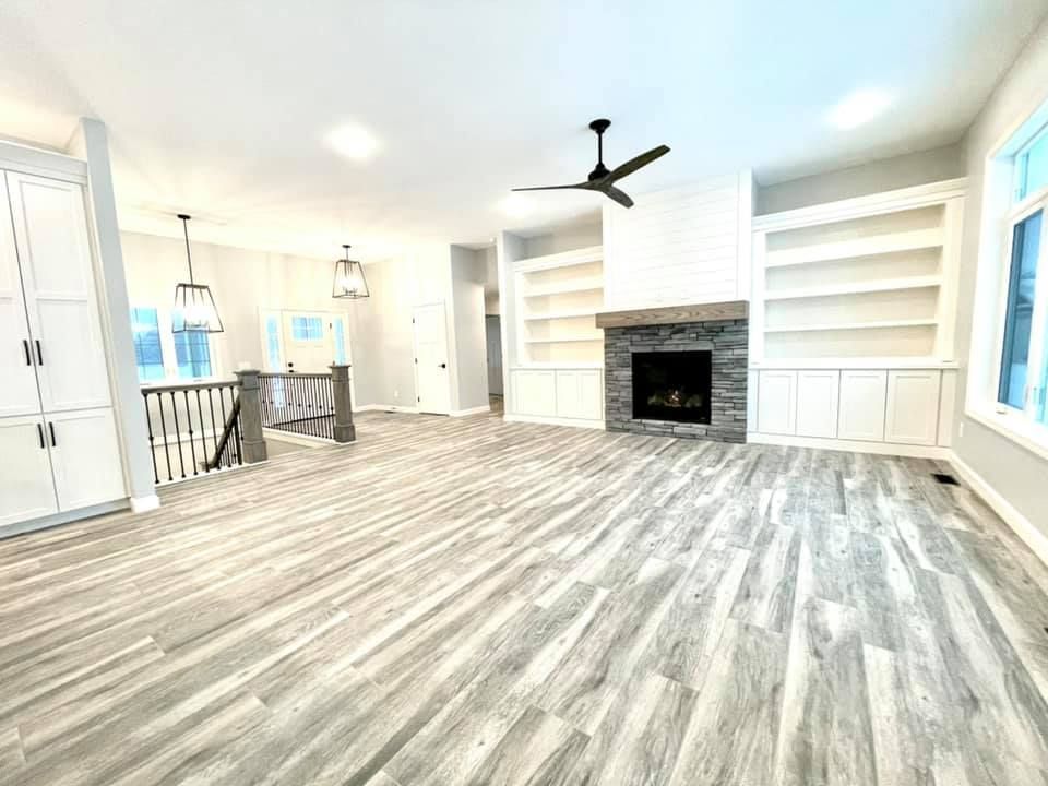 Bright, empty living room with light wood floors, white built-ins, and a stone fireplace.