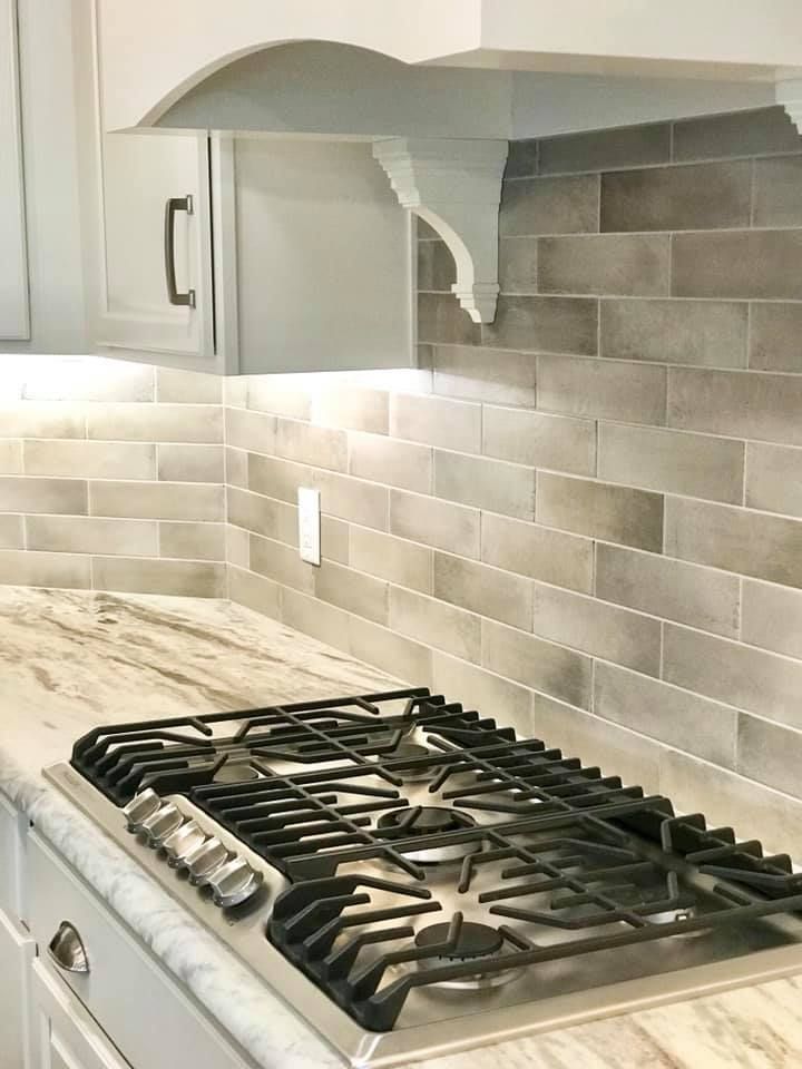Modern kitchen stovetop beneath white range hood, with gray tile backsplash and under-cabinet lighting