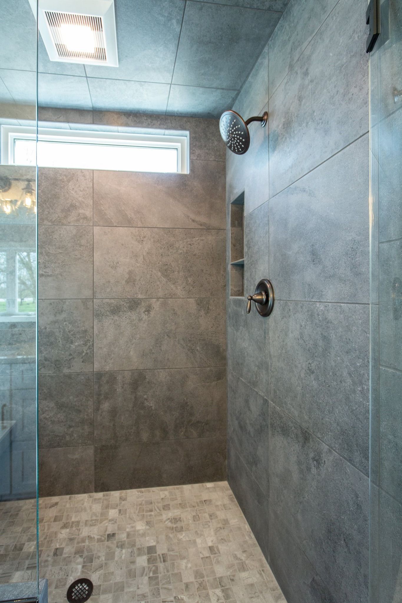 Modern tiled shower with glass door and ceiling vent, no fixtures visible aside from showerheads.
