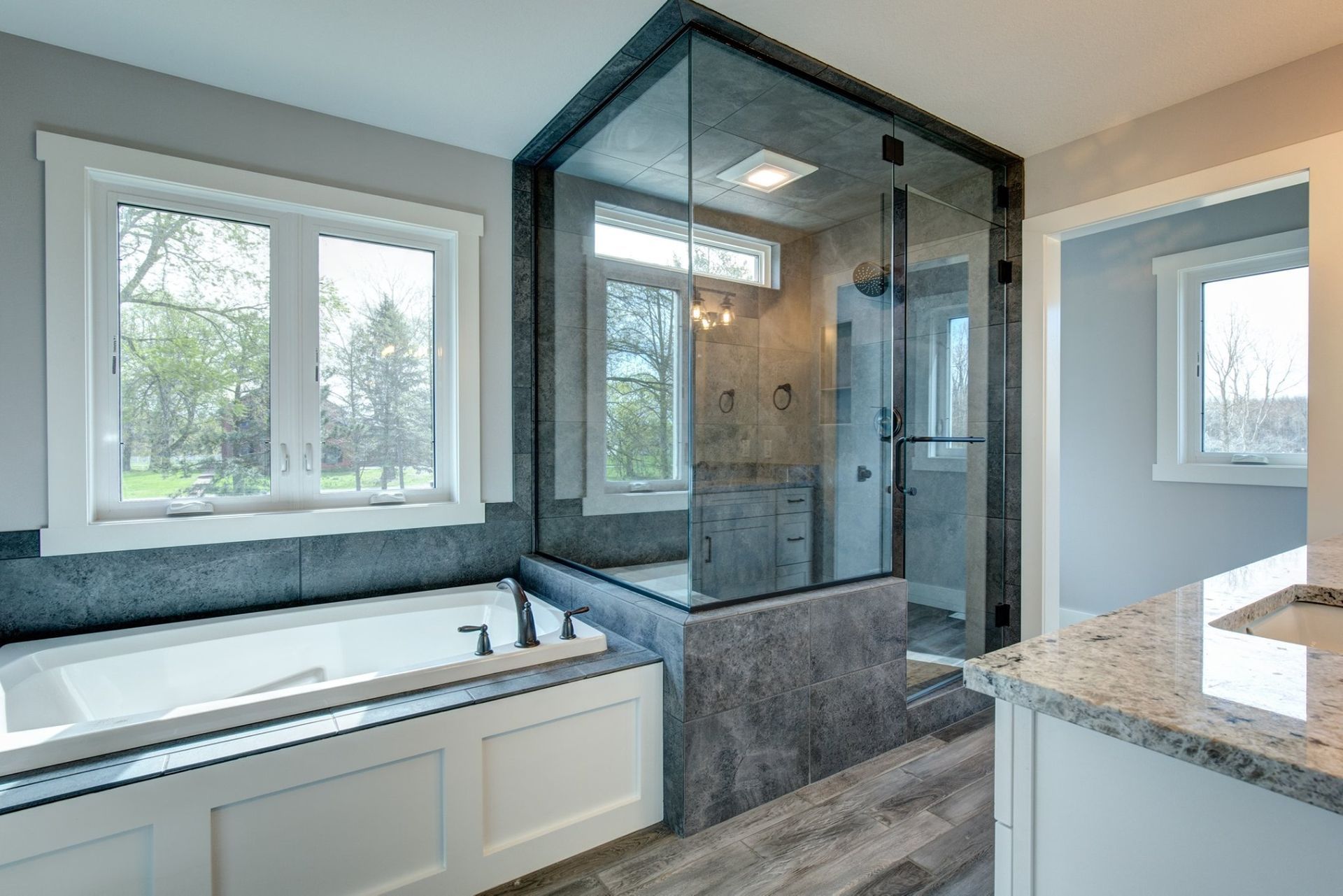 Modern bathroom with freestanding tub, glass shower, gray walls, and white vanity in natural light