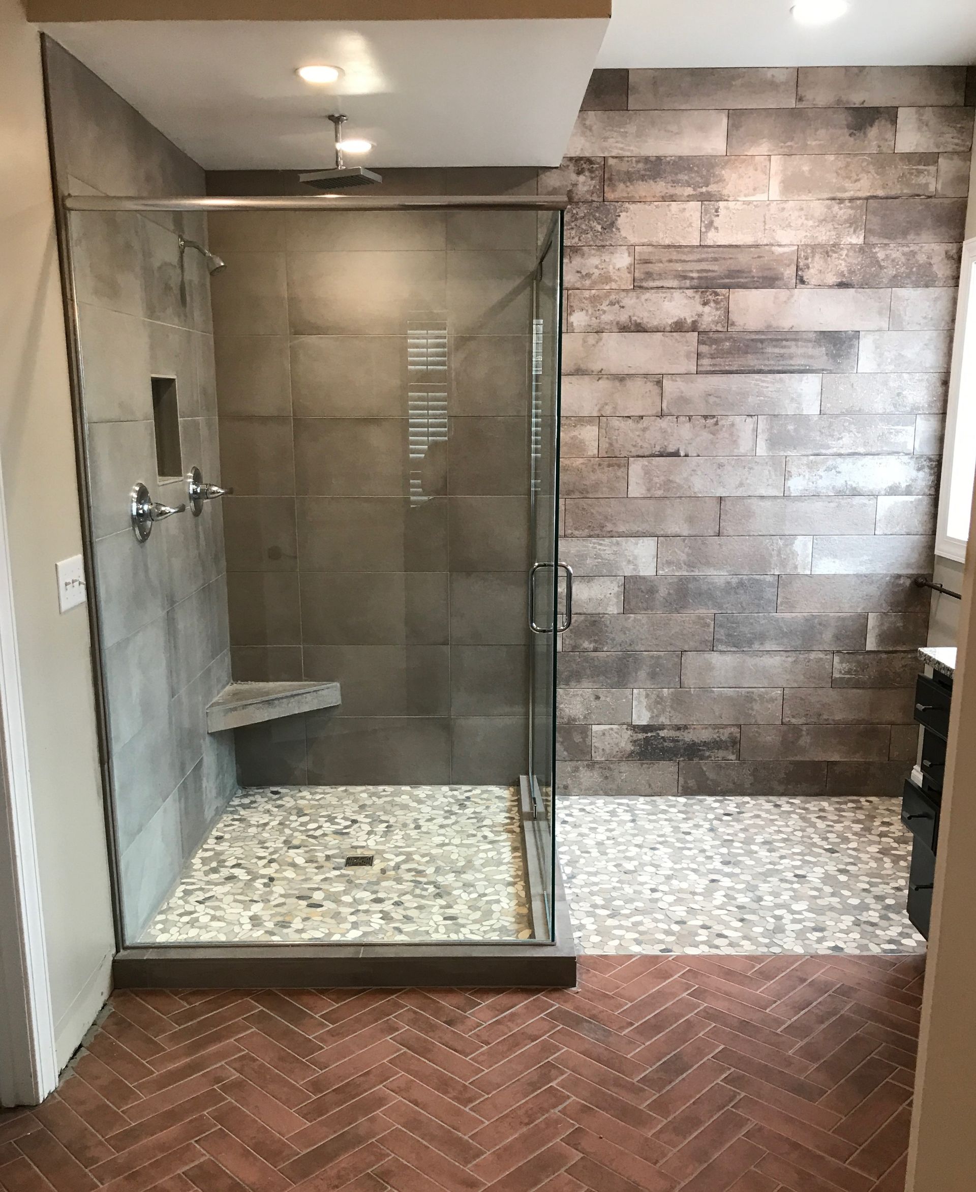 Modern bathroom with glass shower, stone wall, and herringbone wood floor