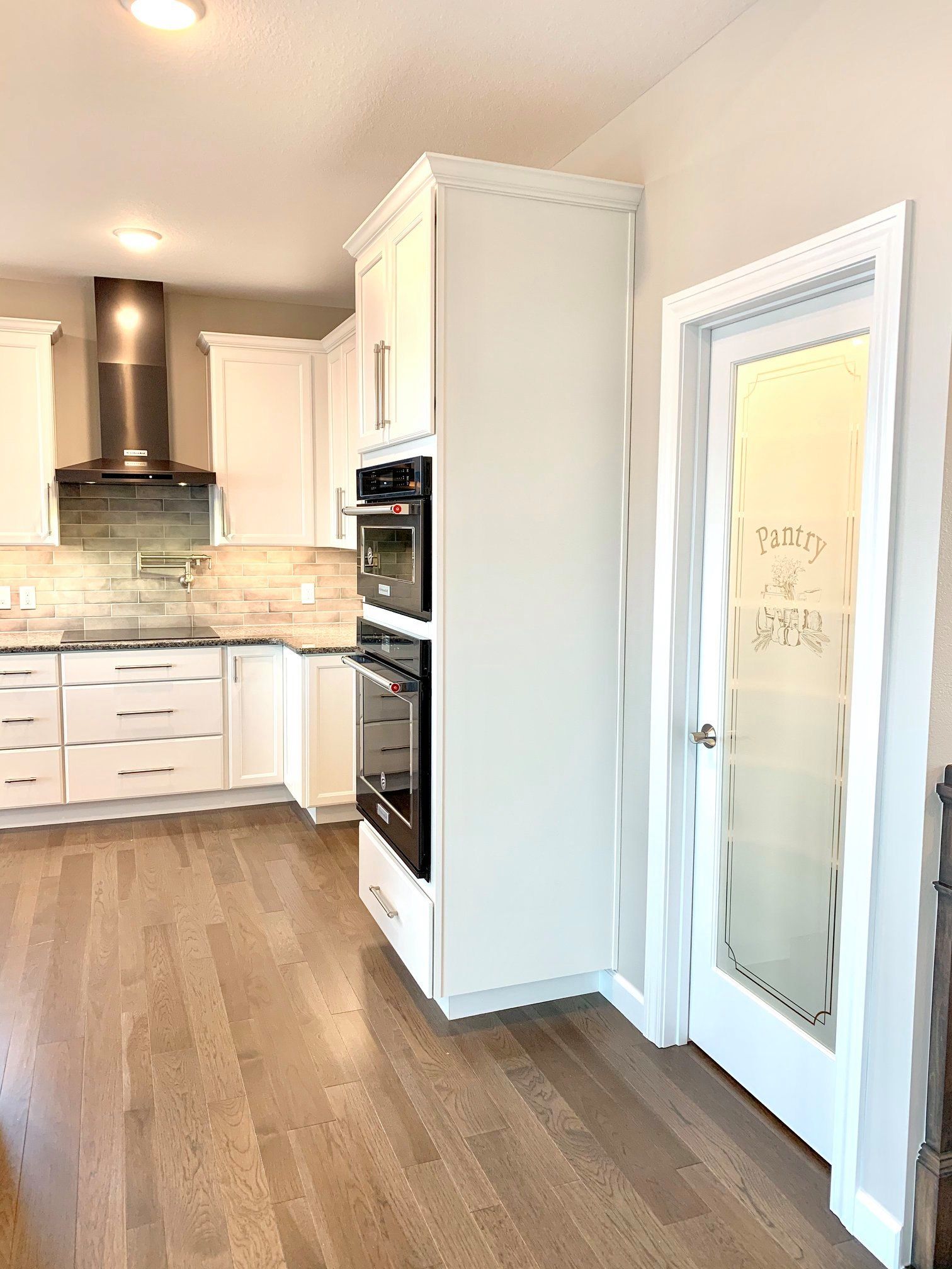 Bright modern kitchen with white cabinets, stainless hood, and frosted glass pantry door on wood floors