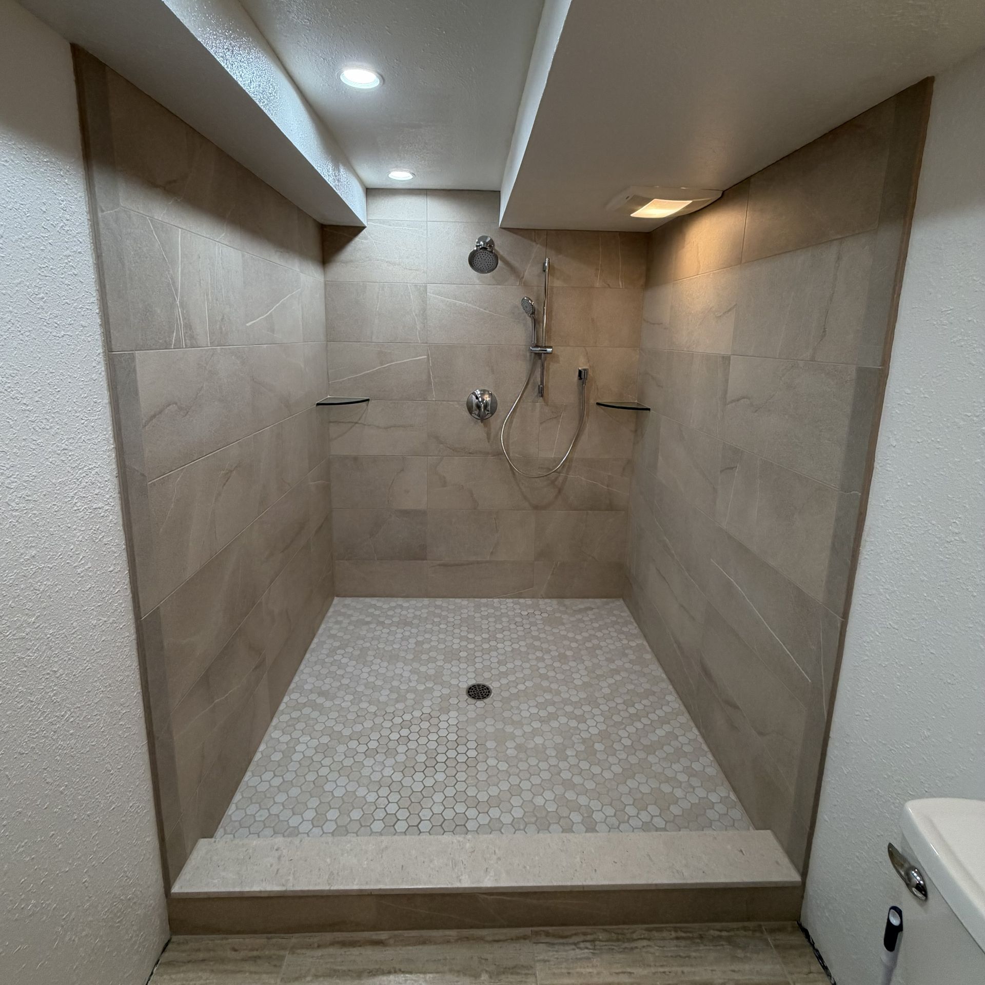 Tiled walk-in shower with handheld showerhead, bench ledge, and mosaic floor drain.