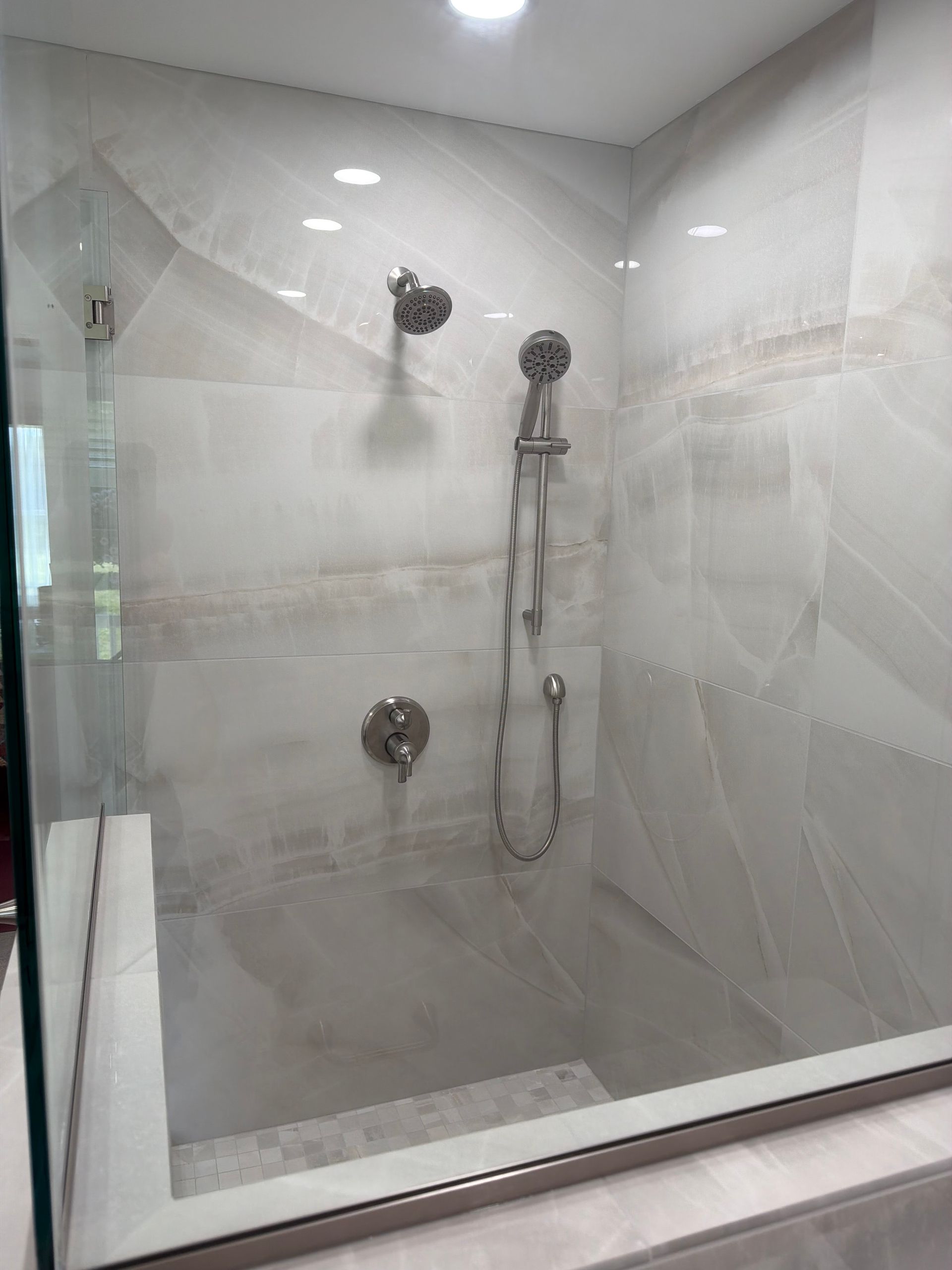 Modern tiled shower with glass door, handheld showerhead, and wall-mounted fixtures
