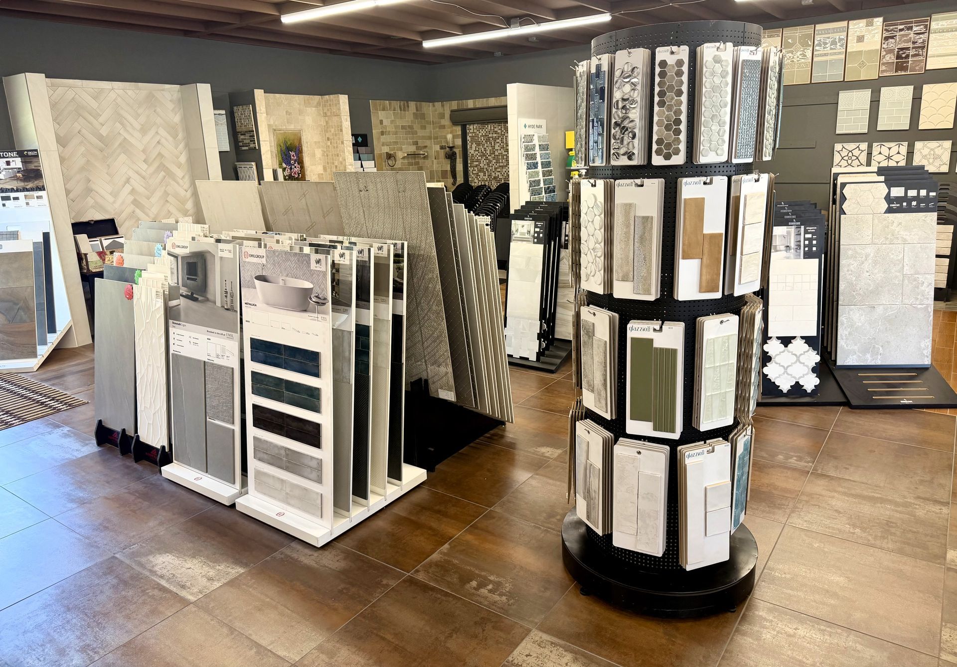 Tile showroom with display racks of patterned tiles and flooring samples on a wood floor.