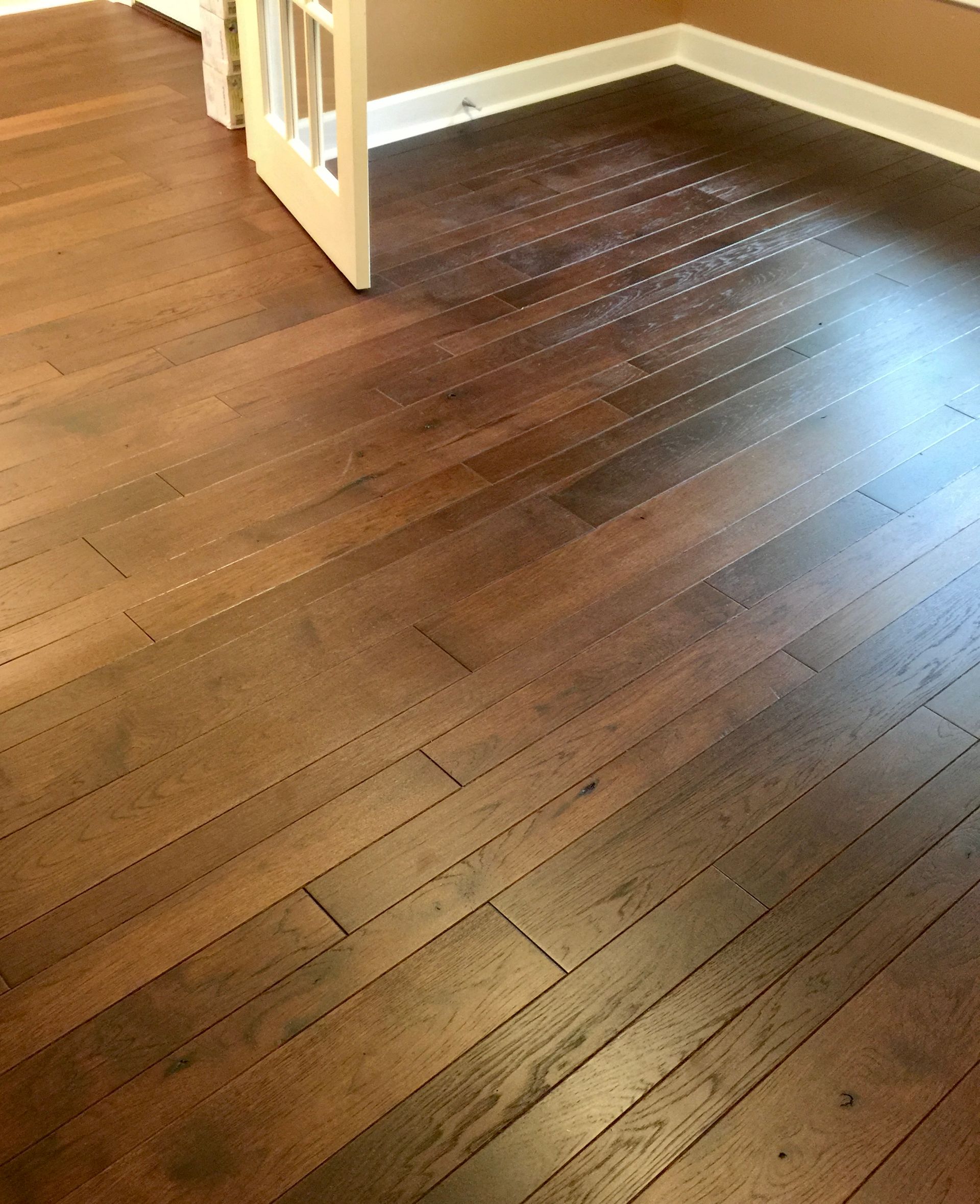 Dark hardwood floor in an empty room with a white baby gate and tan walls.