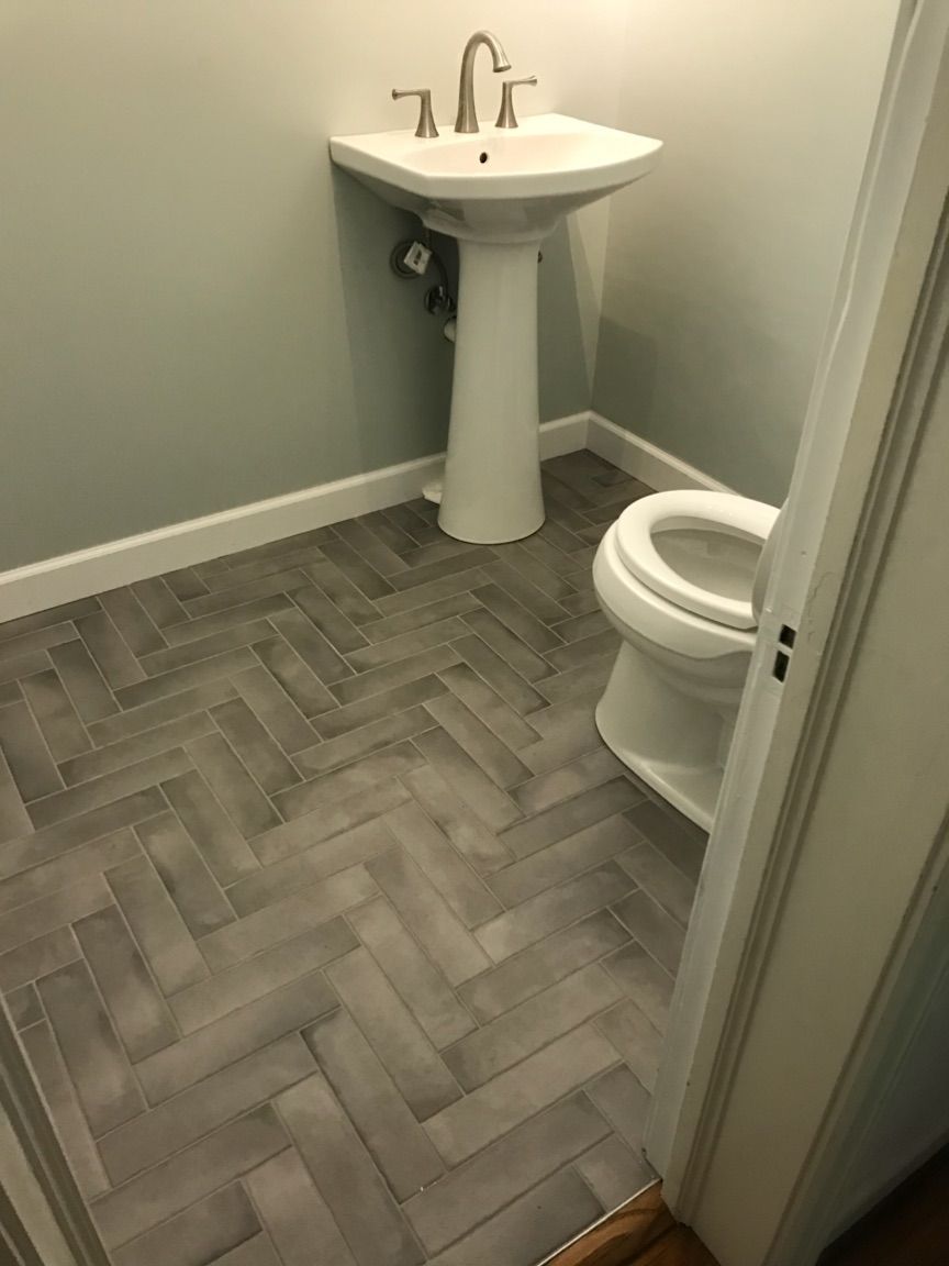 Small bathroom with gray herringbone tile, white pedestal sink, and toilet by the door.