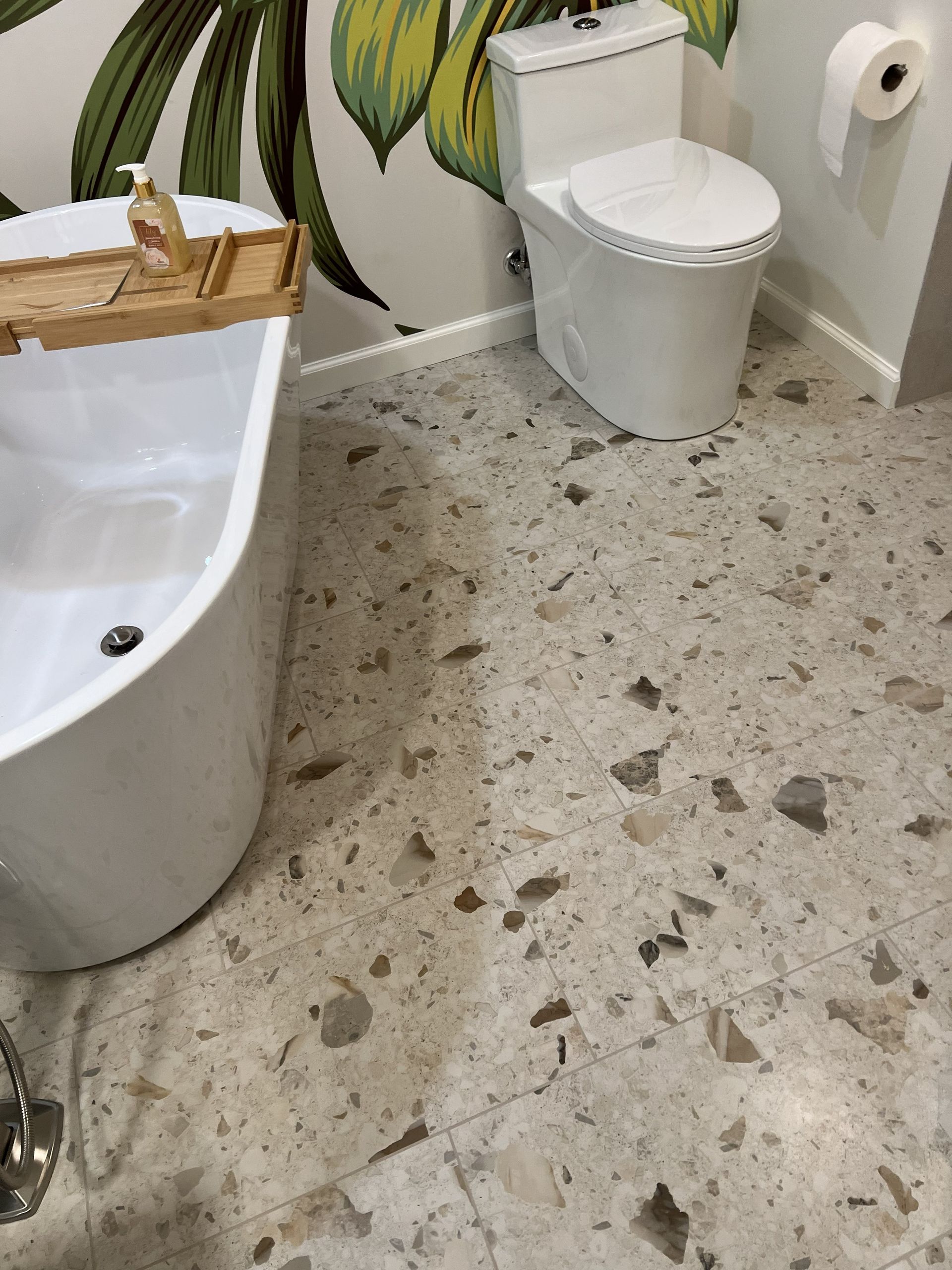 Small bathroom with a toilet, bathtub, toilet paper roll, and speckled floor with water spots.