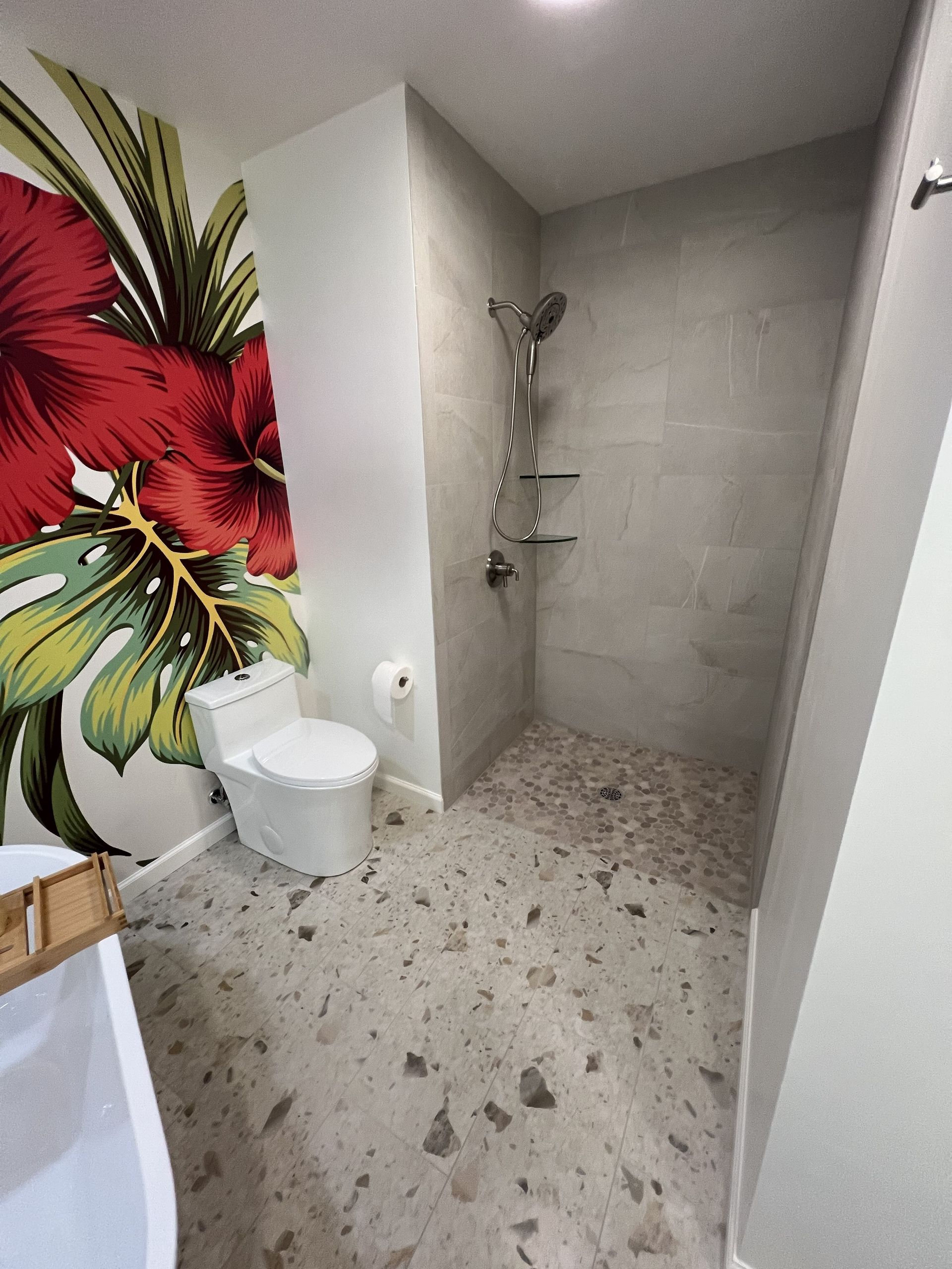 Small bathroom with shower, toilet, and tropical floral wall mural on the left.