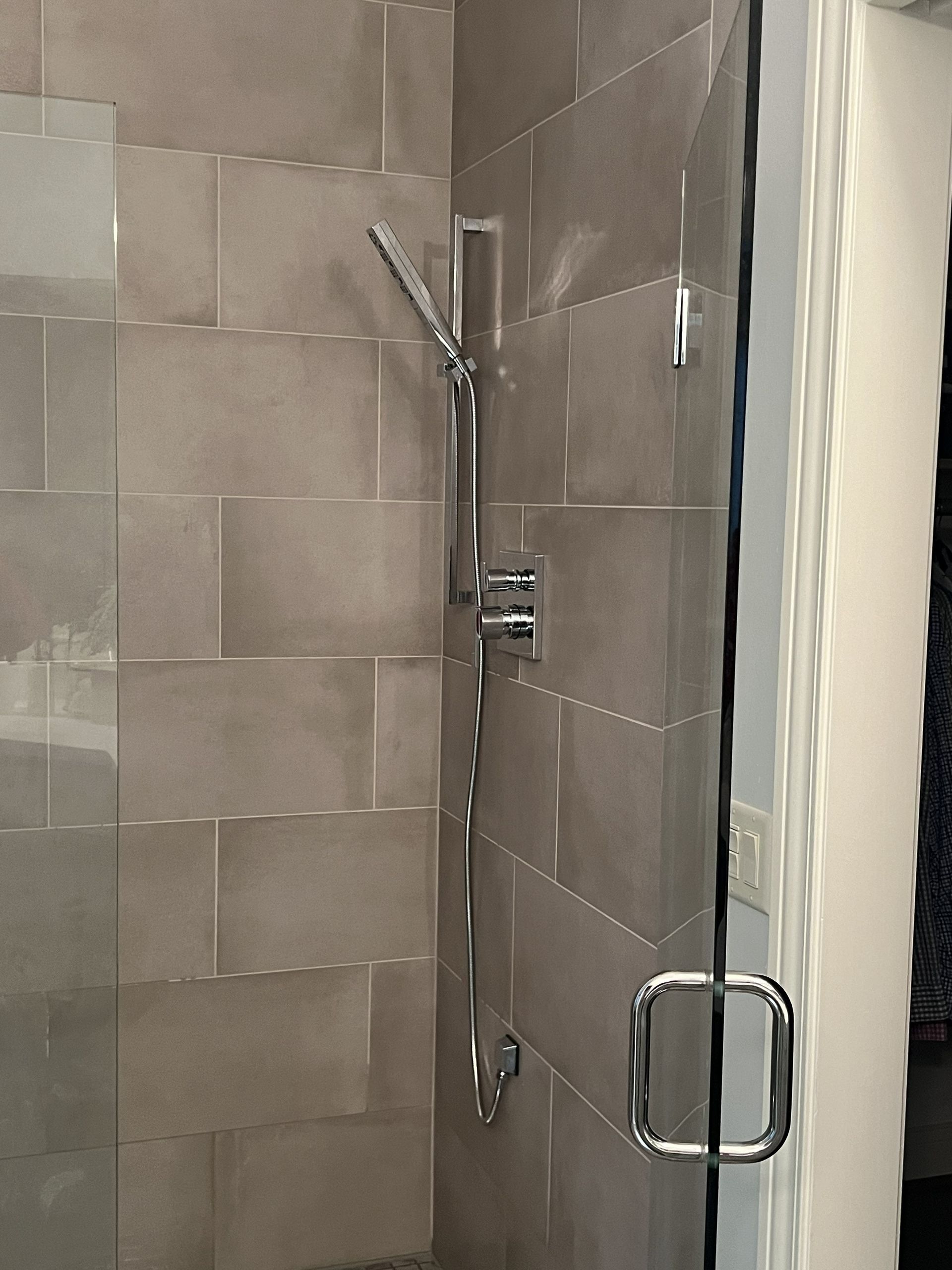 Walk-in shower with gray tile walls, chrome shower fixtures, and a clear glass door handle.