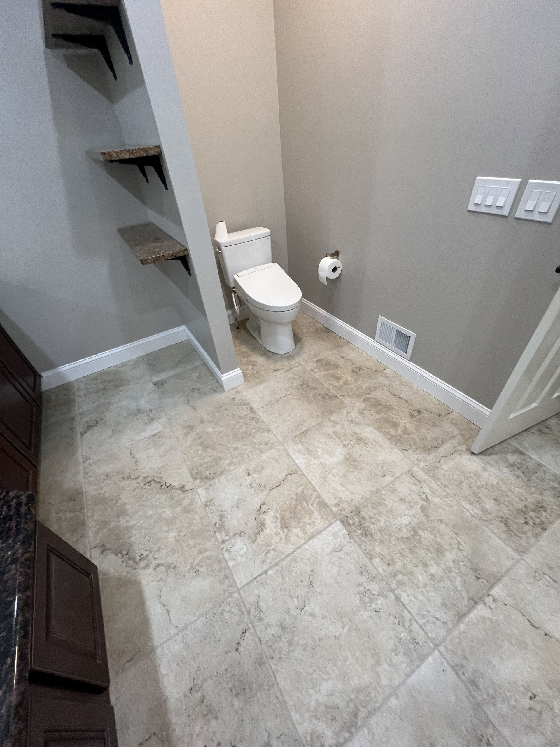 Small tiled bathroom with a toilet, gray walls, and built-in corner shelves.