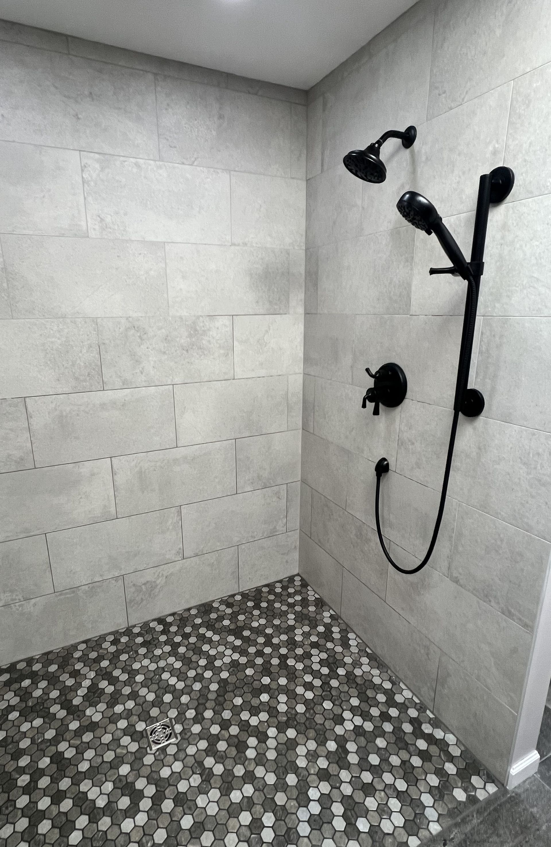 Modern tiled shower with black fixtures and patterned pebble-style floor.
