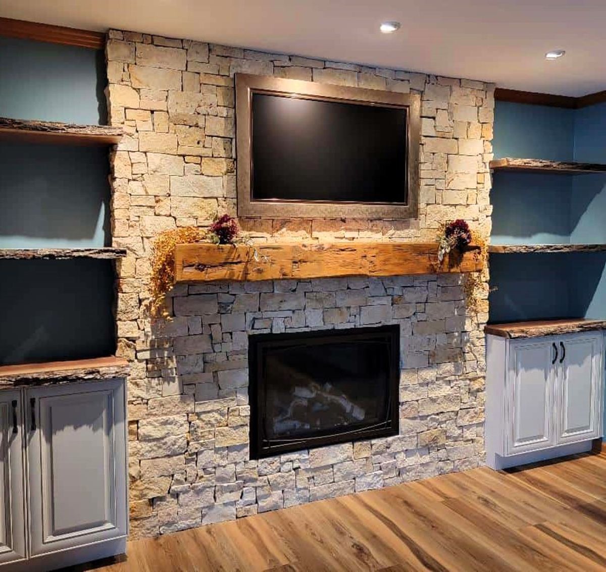 Stone fireplace wall with a TV above, black insert, built-in cabinets, and wood flooring in a living room