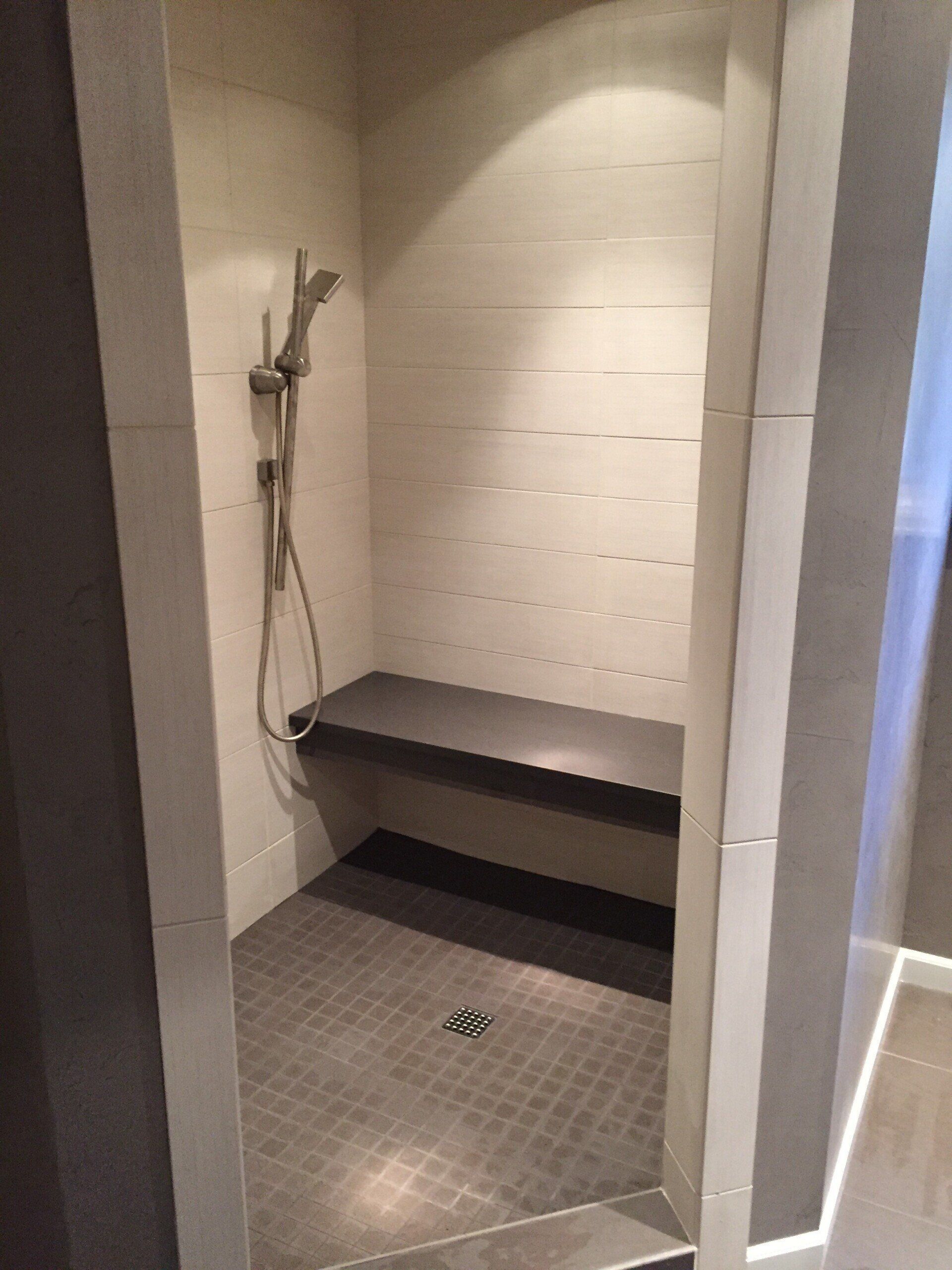 Small tiled shower stall with a bench and handheld showerhead in a modern bathroom