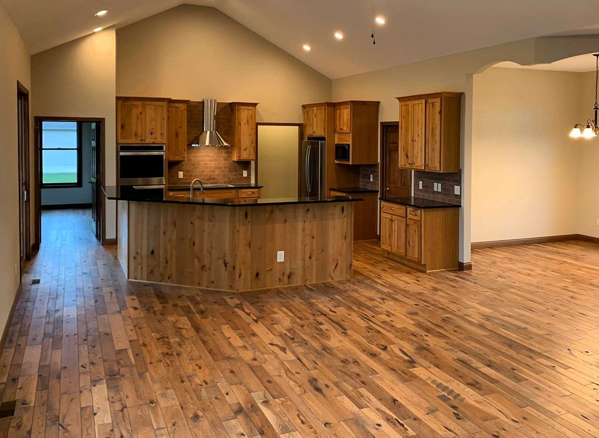 Spacious empty kitchen and open living area with wood floors, wooden cabinets, and vaulted ceiling