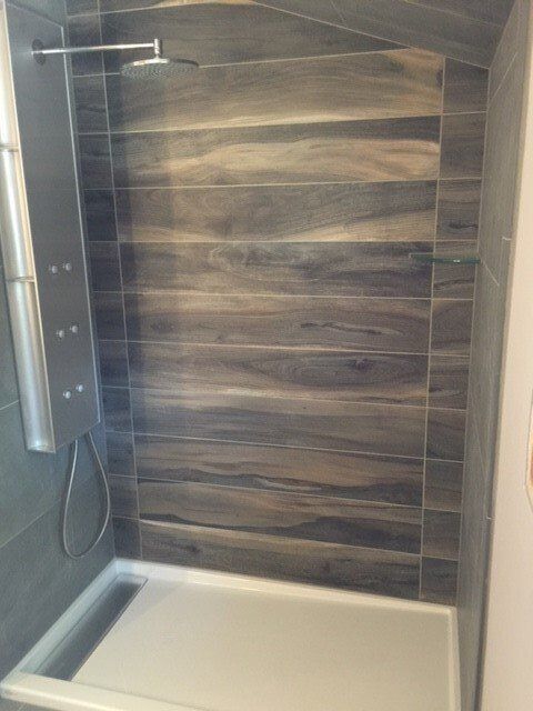 Modern walk-in shower with wood-look wall tiles, white tub base, and chrome fixtures