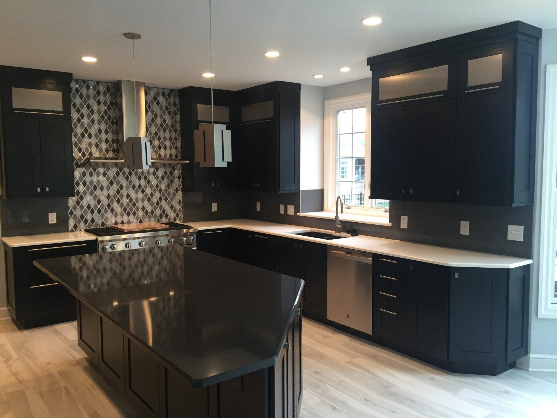 Modern kitchen with dark cabinets, black island, white countertops, and tiled backsplash
