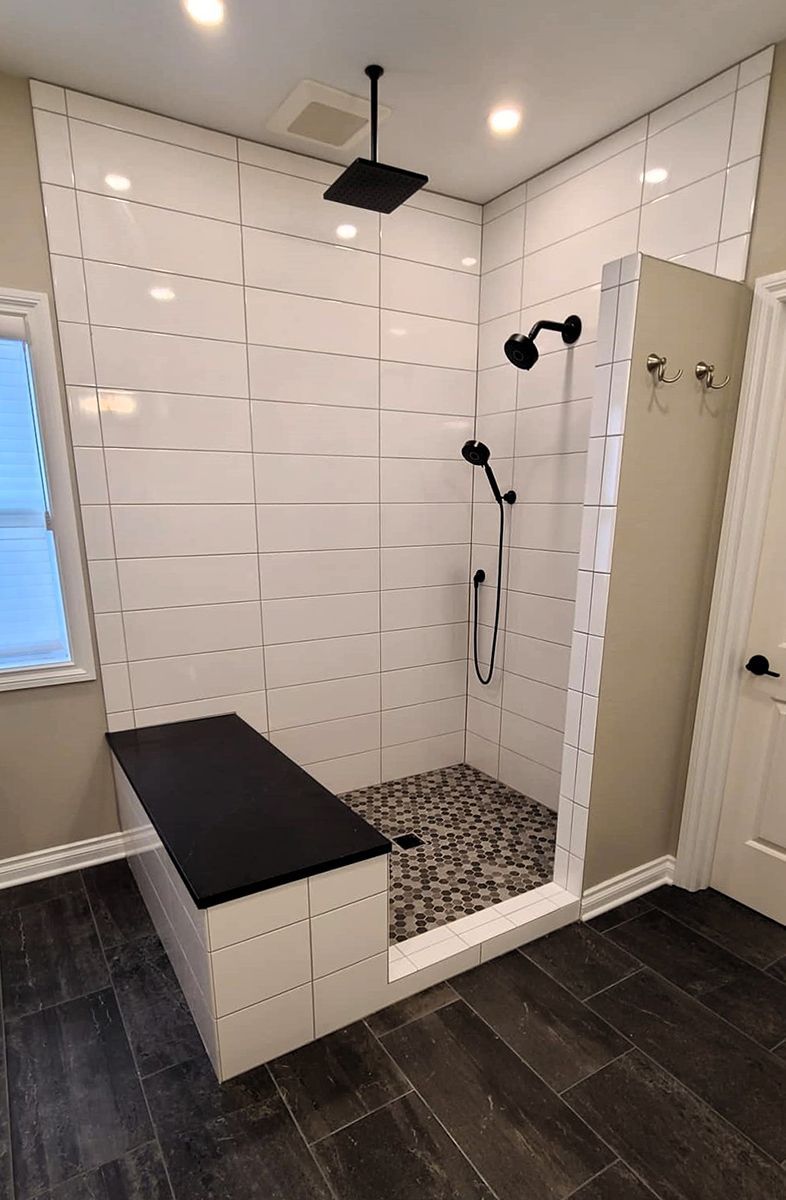 Modern white-tiled walk-in shower with black fixtures, bench, and dark wood flooring