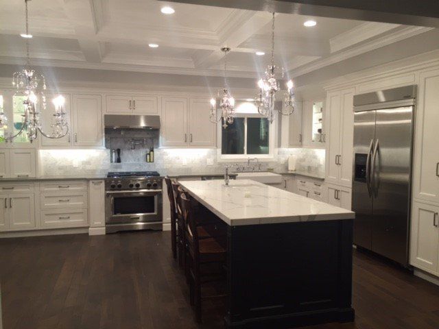 Bright modern kitchen with dark island, white cabinets, stainless steel appliances, and hardwood floors