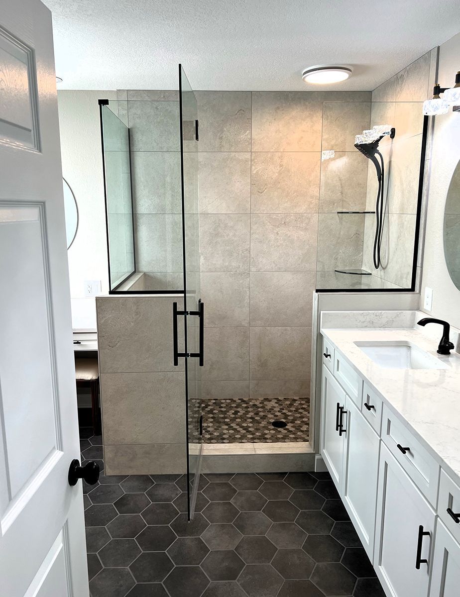 Modern bathroom with glass walk-in shower, black hex tile floor, white vanity, and tiled walls