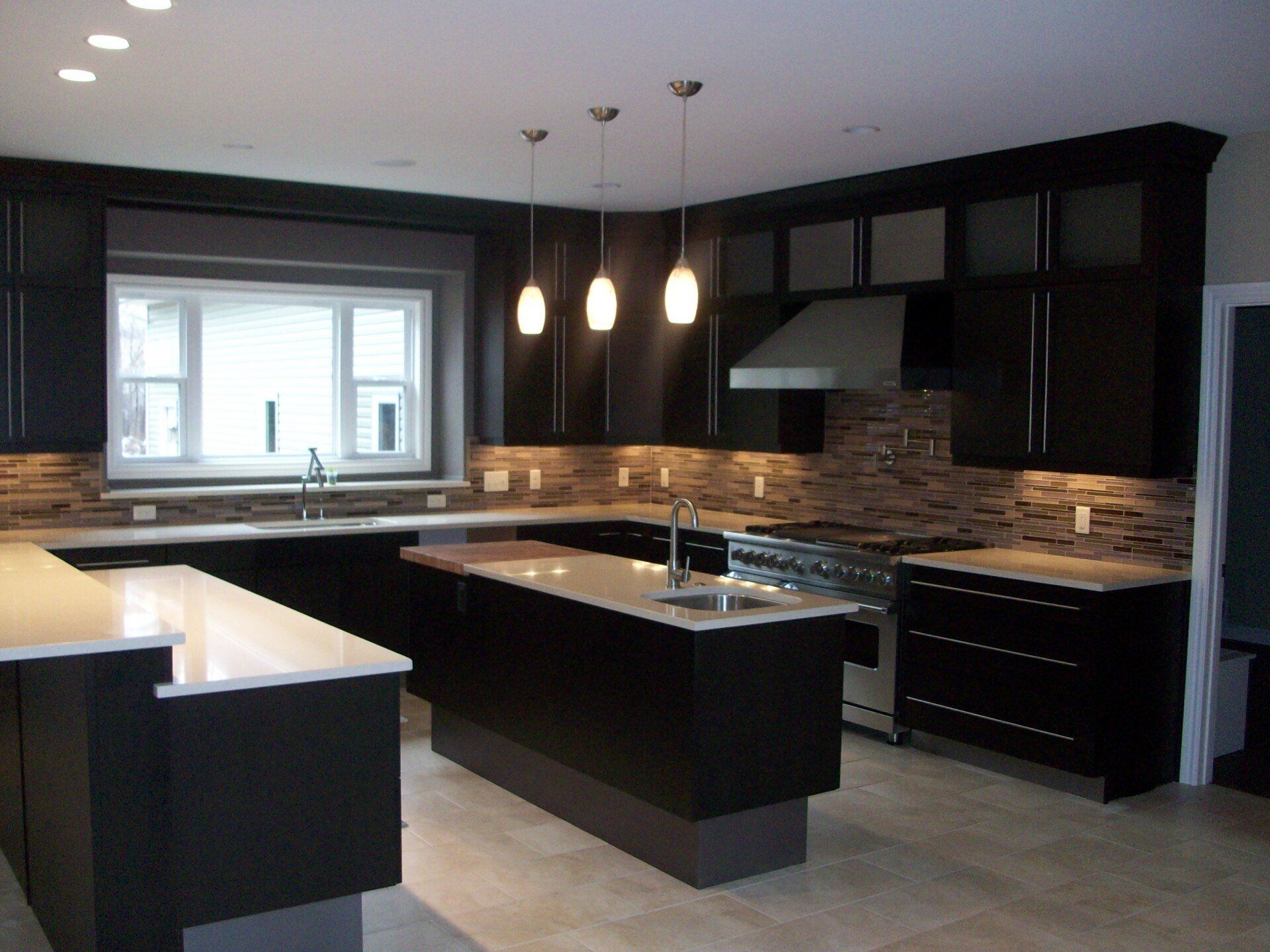 Modern kitchen with dark cabinets, central island, pendant lights, and a window over the sink.