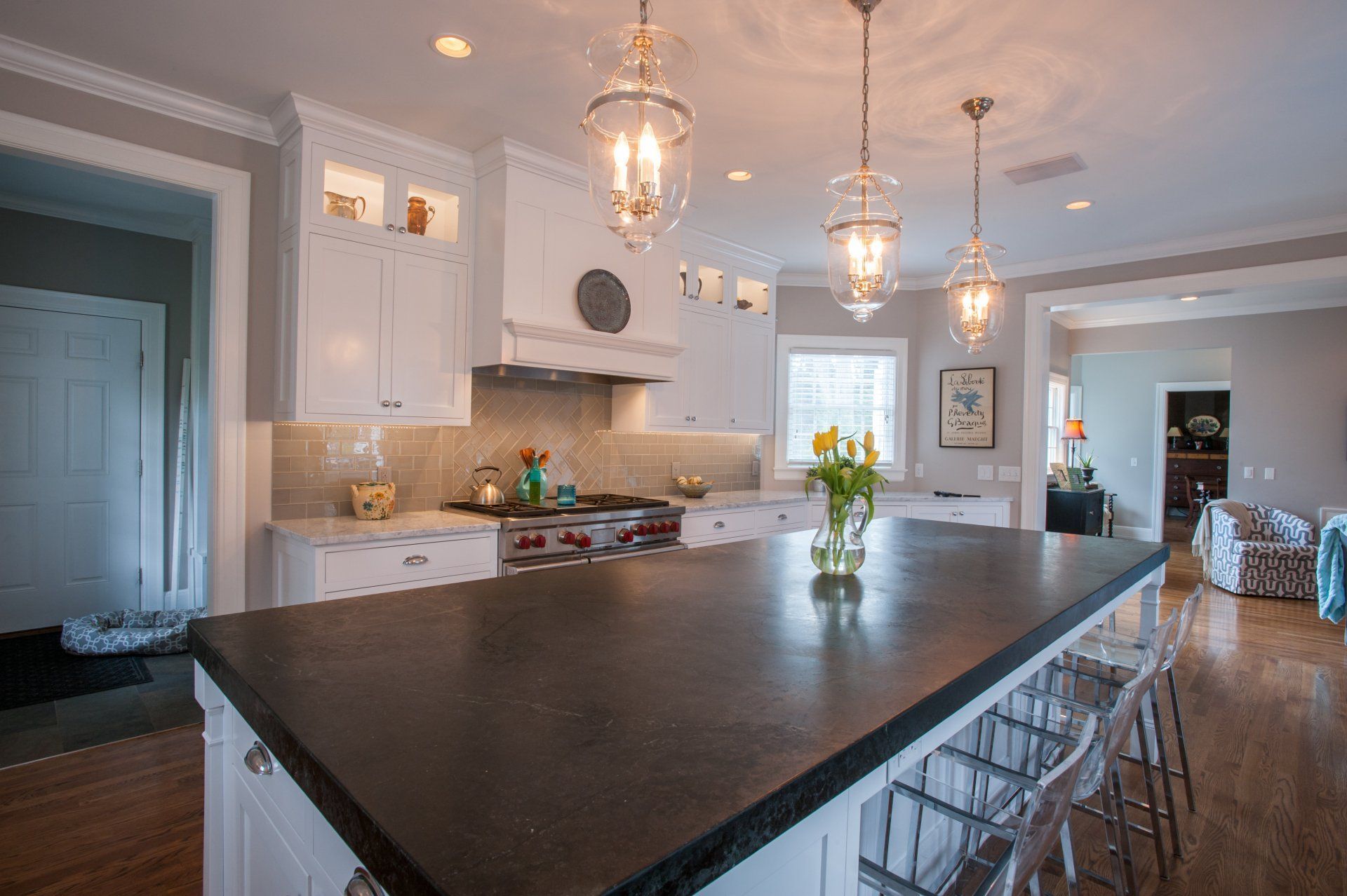 Modern kitchen with a large black island, white cabinets, pendant lights, and stainless-steel range hood.