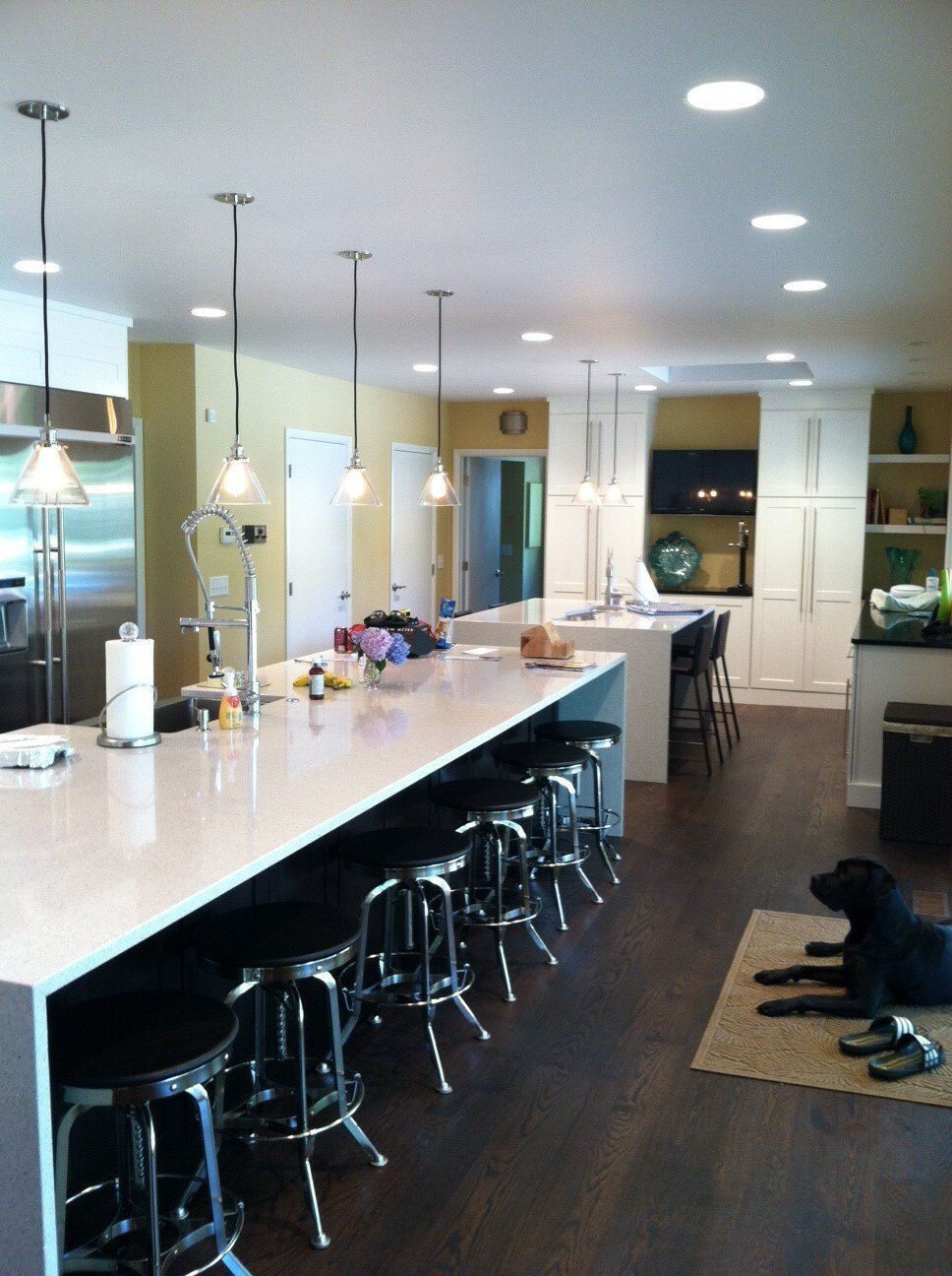 Bright kitchen with a long island, bar stools, pendant lights, and a dog resting on a rug near the counter.